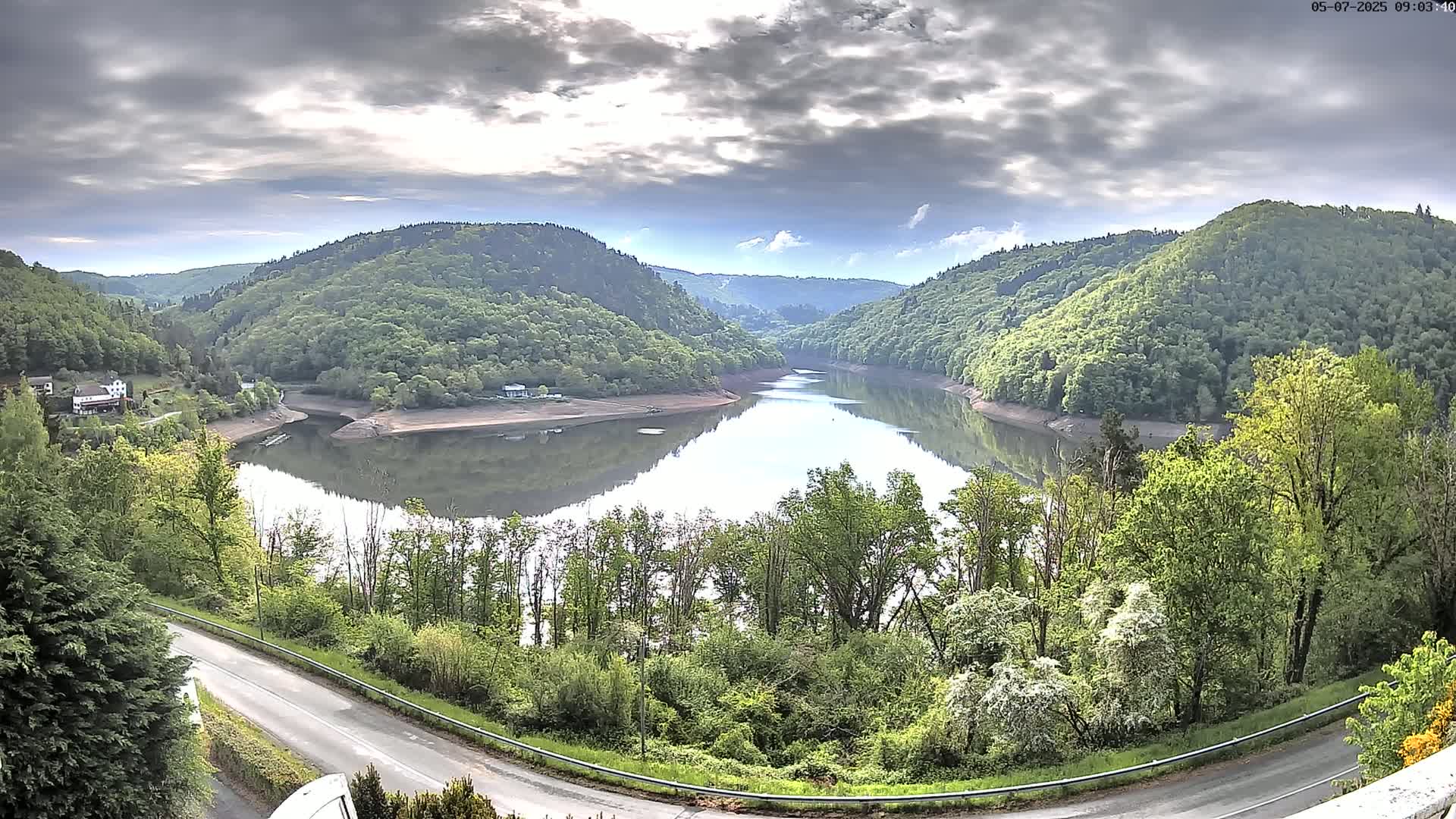 A calm lake nestled between lush green hills under a partly cloudy sky.