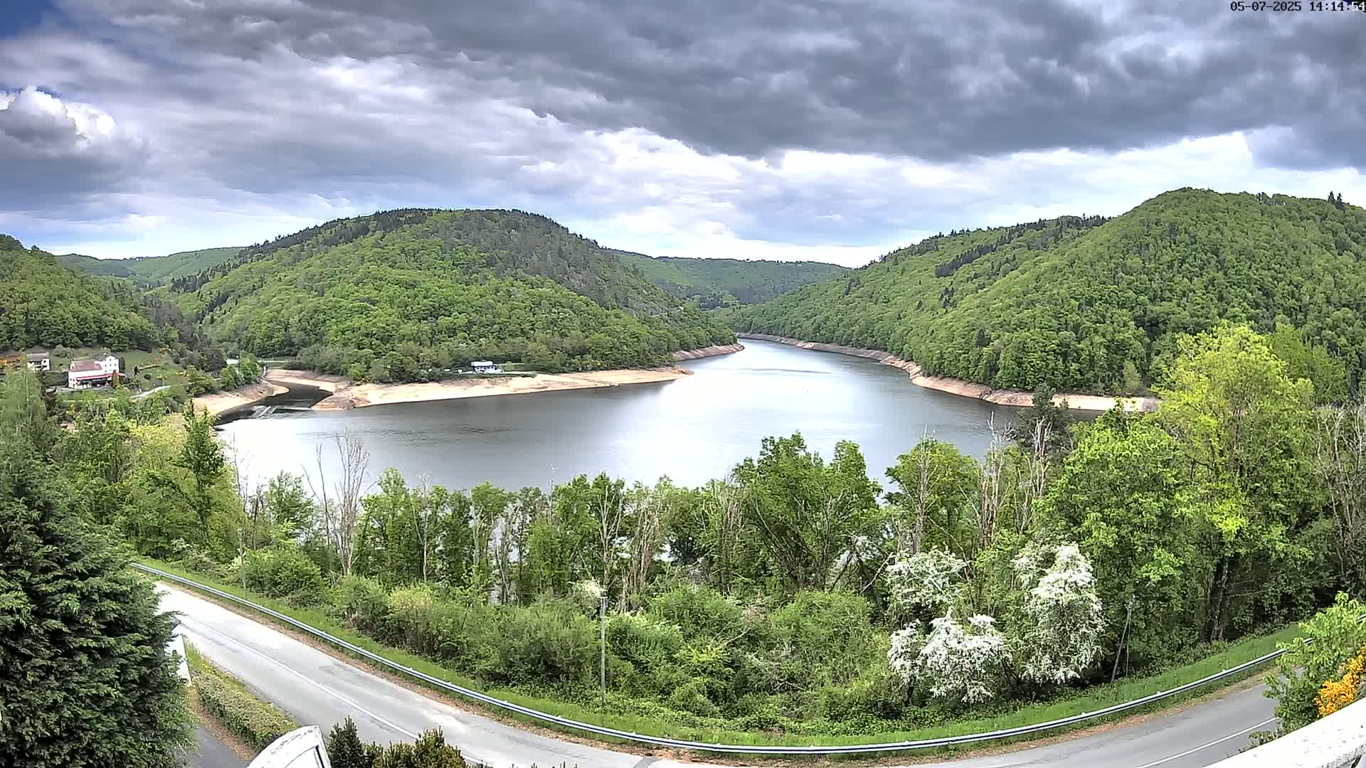 A winding reservoir nestled in a valley of lush green hills under a cloudy sky.