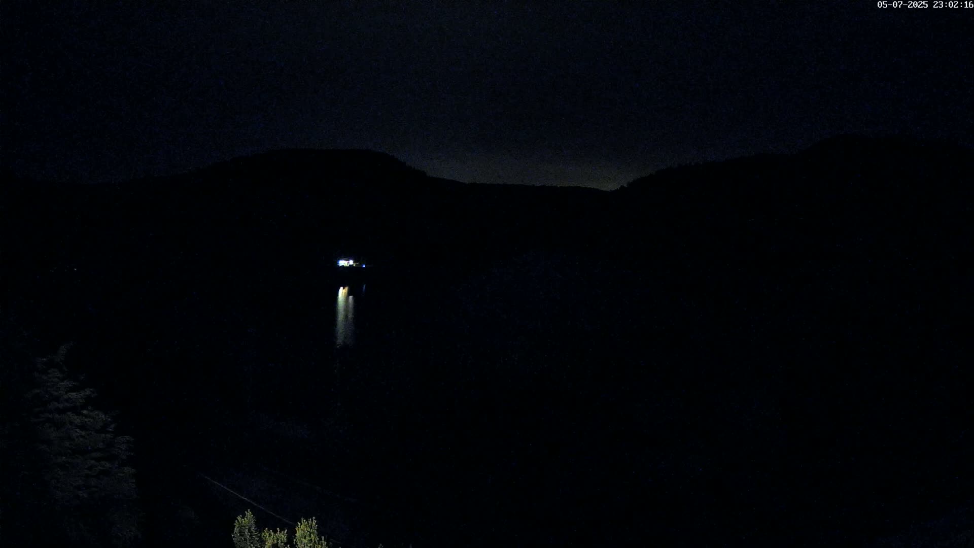 A dimly lit building is visible in the distance on a dark, nighttime landscape with a hill in the background.