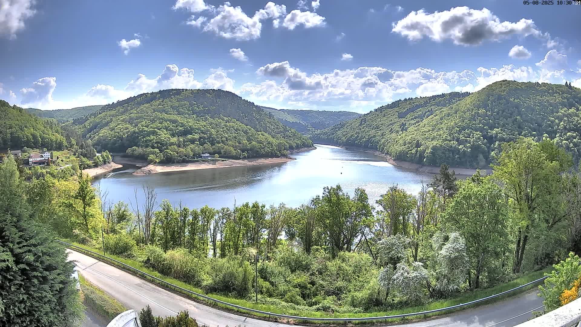 A winding river flows through a lush green valley under a partly cloudy sky.