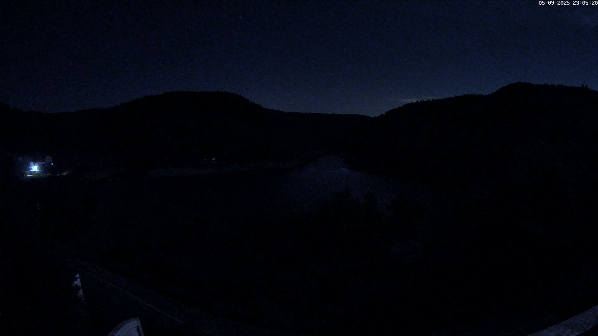 A dark nighttime landscape shows silhouetted hills and a body of water under a clear, dark sky.