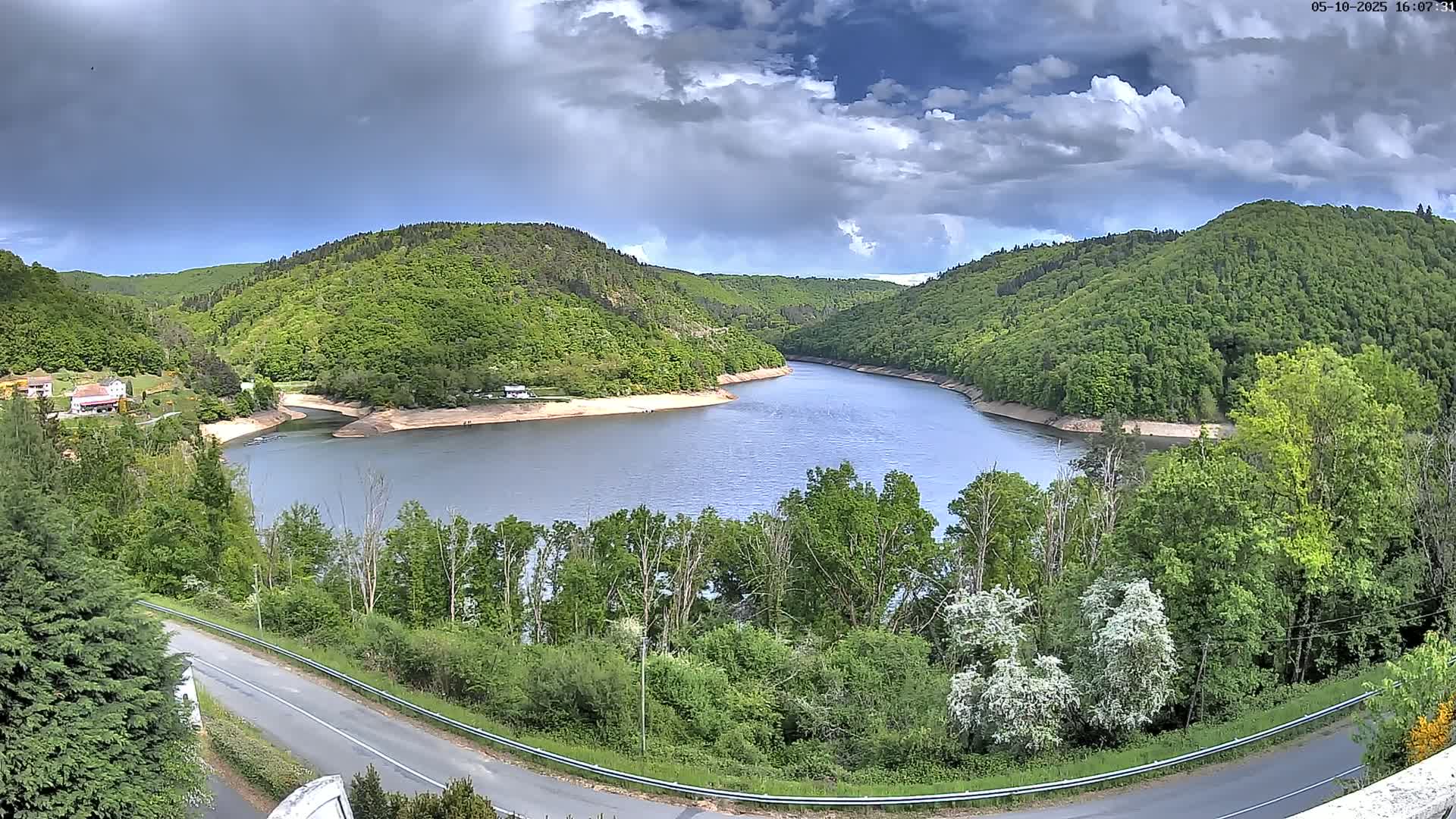 A winding river flows through a lush green valley under a partly cloudy sky.