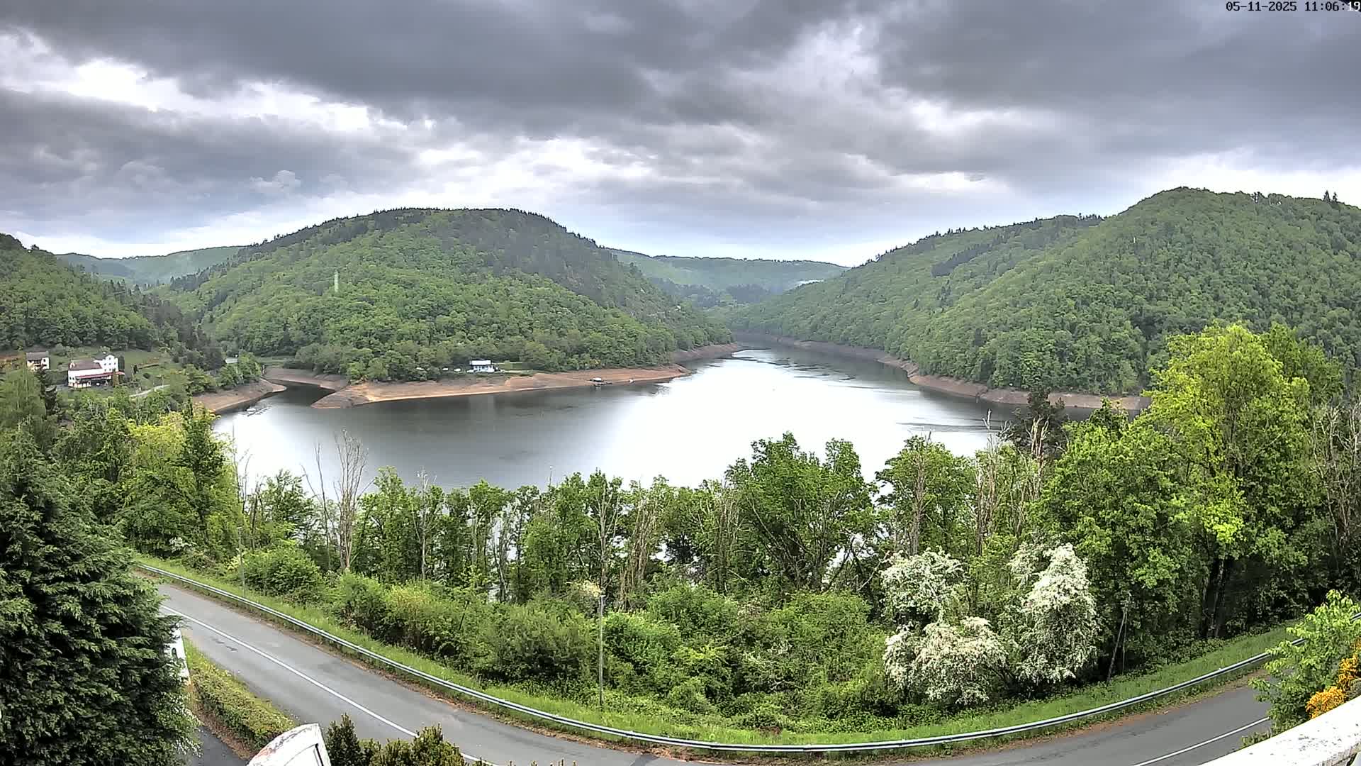 A calm lake nestled in a valley of lush green hills under a cloudy sky.