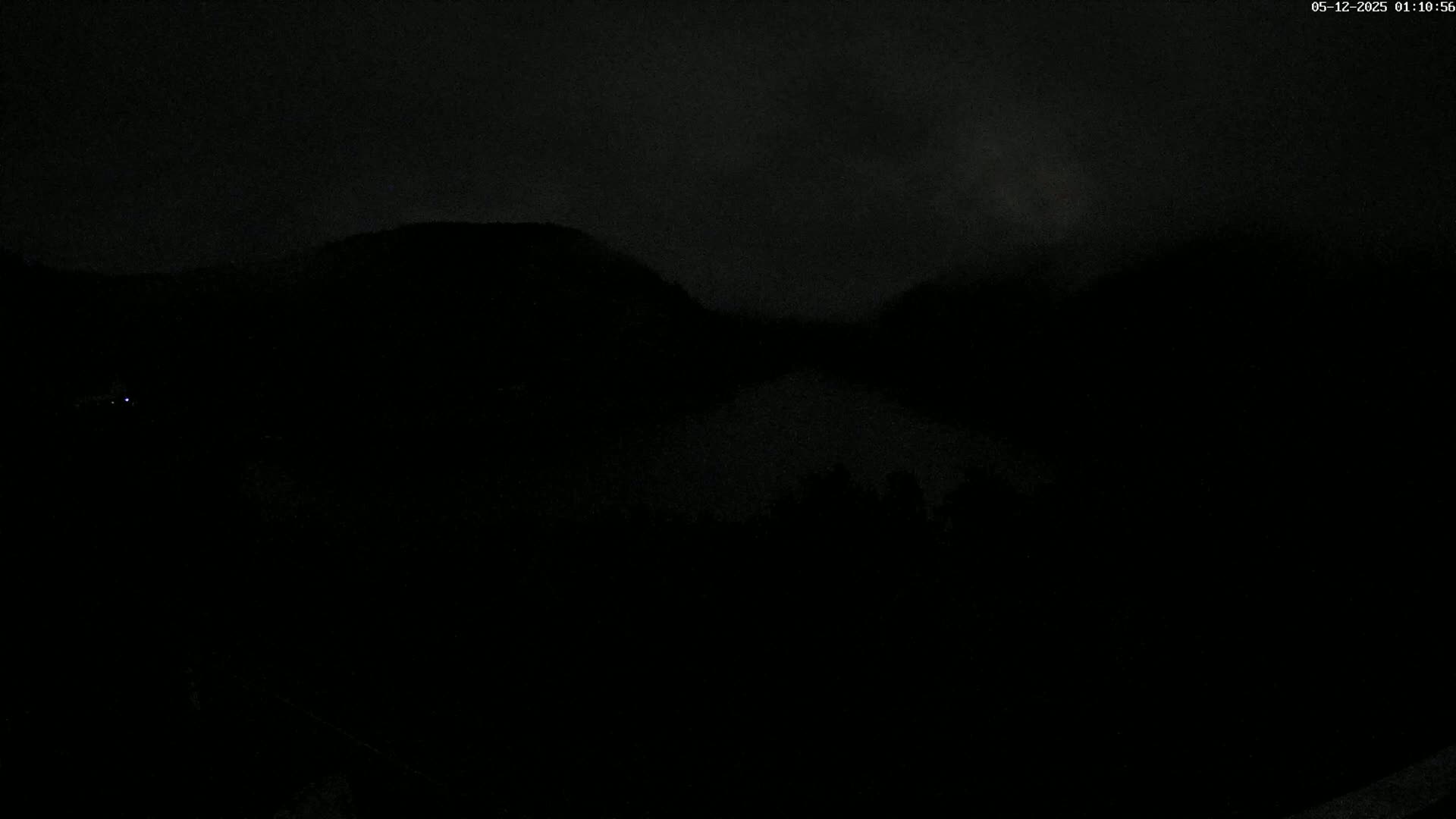 A dark, nighttime scene shows a body of water nestled between hills under a cloudy sky.