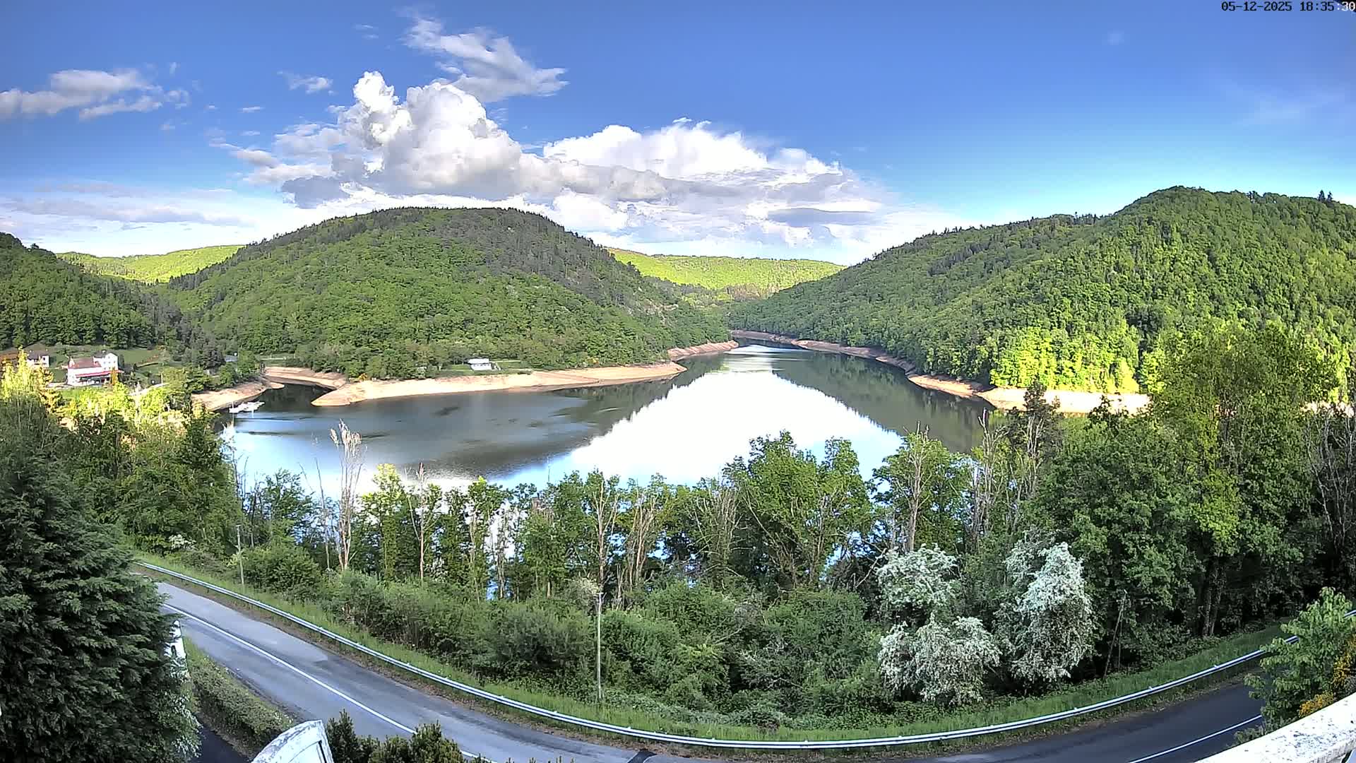 A calm lake nestled in a valley of lush green hills under a partly cloudy blue sky.