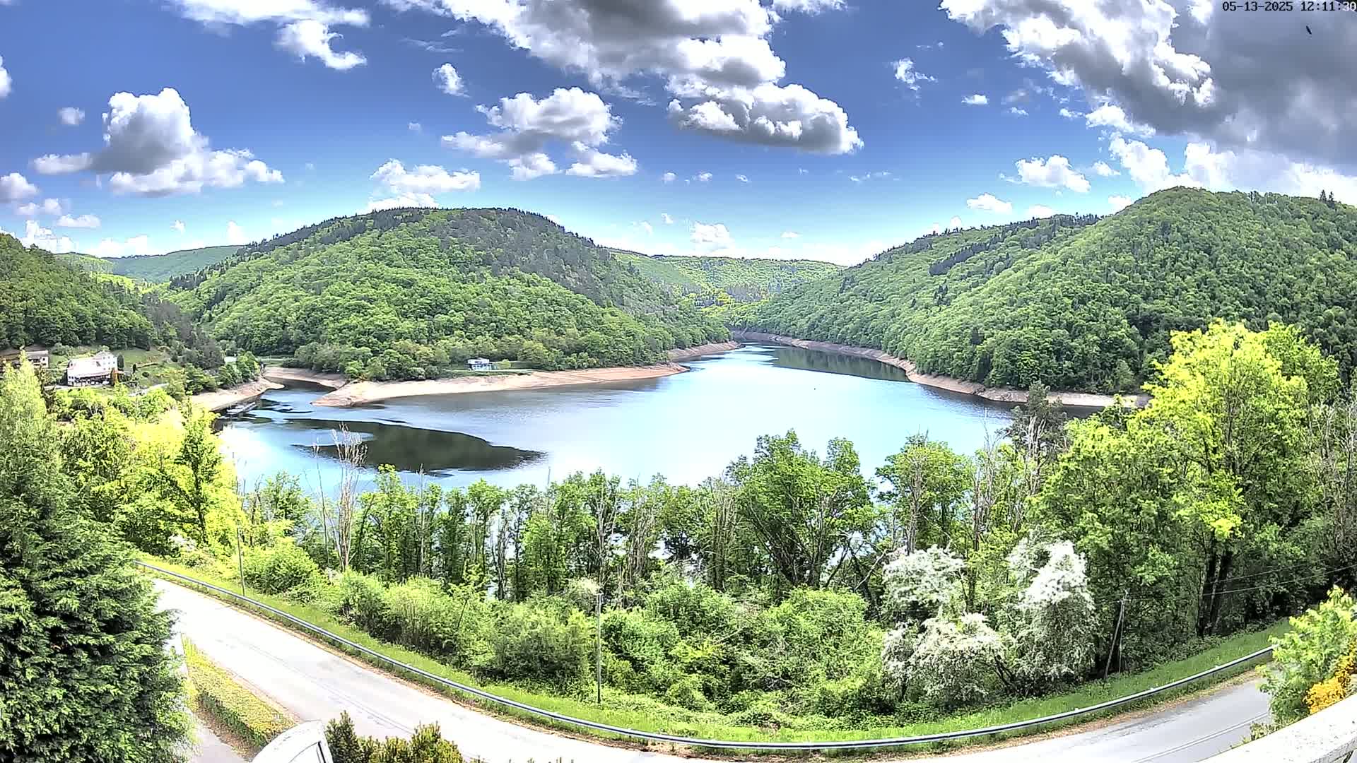 A partly cloudy blue sky overlooks a tranquil lake nestled between lush green hills.