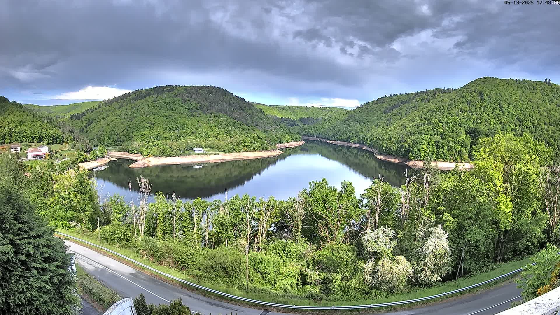 A calm, horseshoe-shaped lake nestled between lush green hills under a partly cloudy sky.