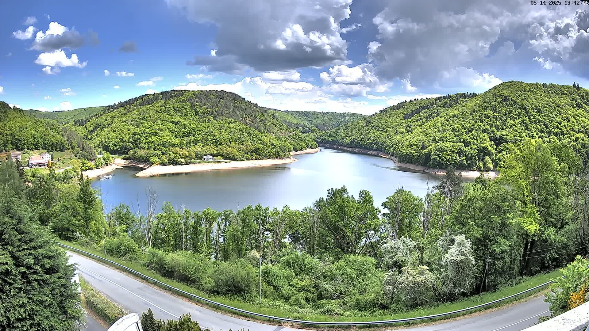 A partly cloudy sky overlooks a winding river surrounded by lush green hills and a road curving through the landscape.