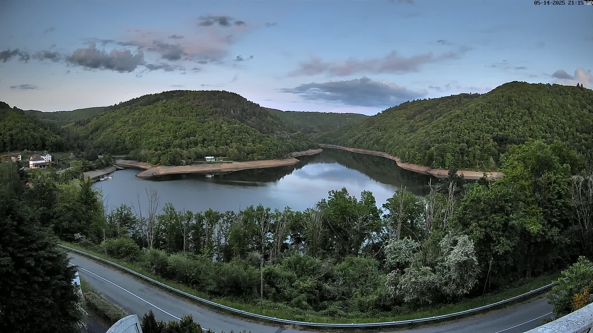 A calm lake nestled between lush green hills under a partly cloudy sky.
