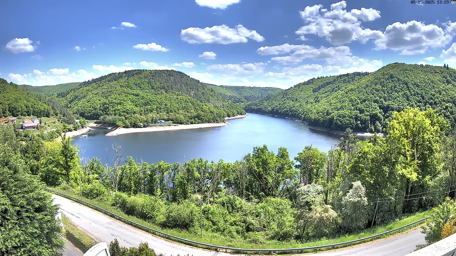 A winding river flows through a lush green valley under a partly cloudy blue sky.
