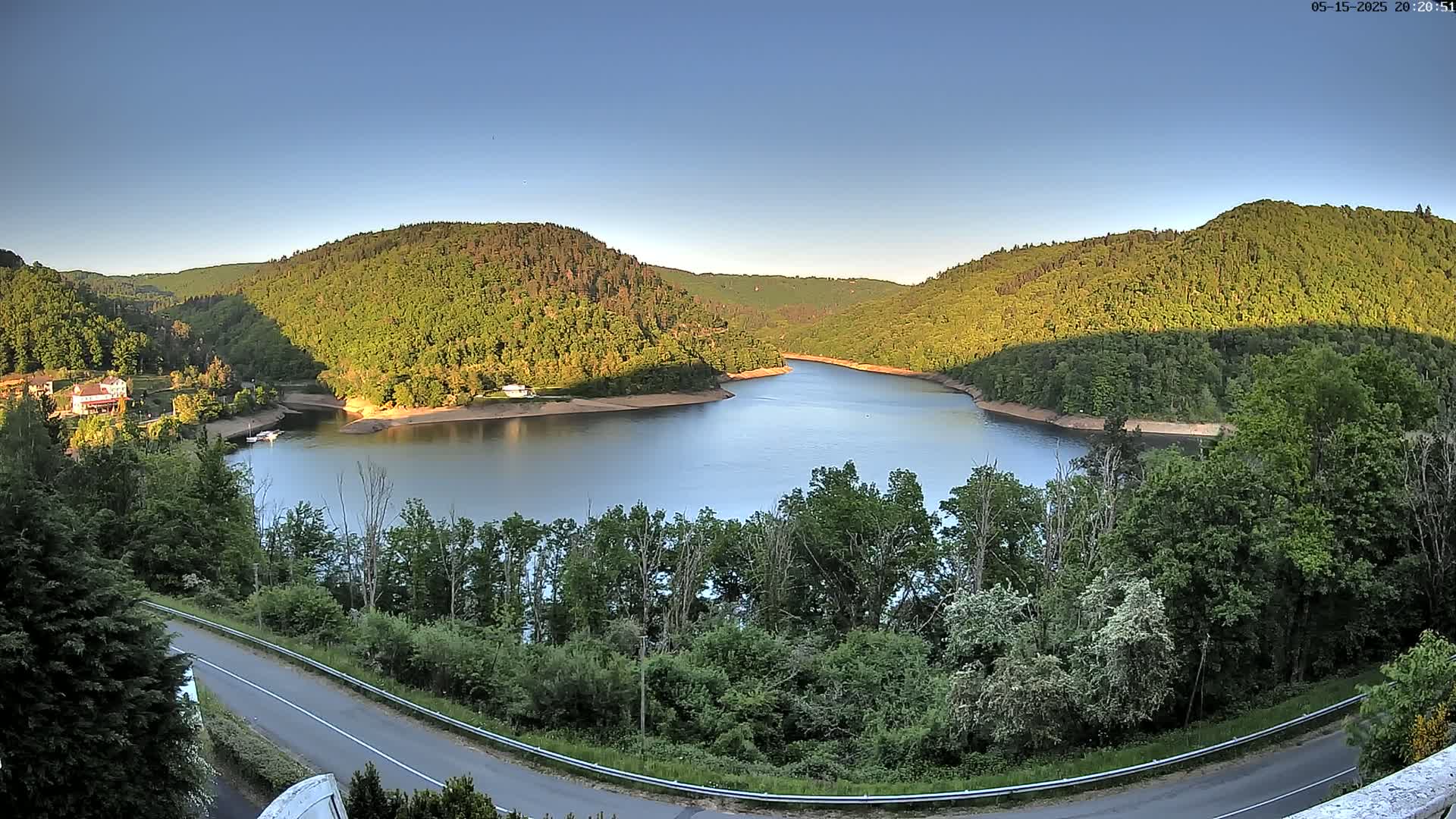 A calm lake nestled between lush green hills under a clear blue sky.