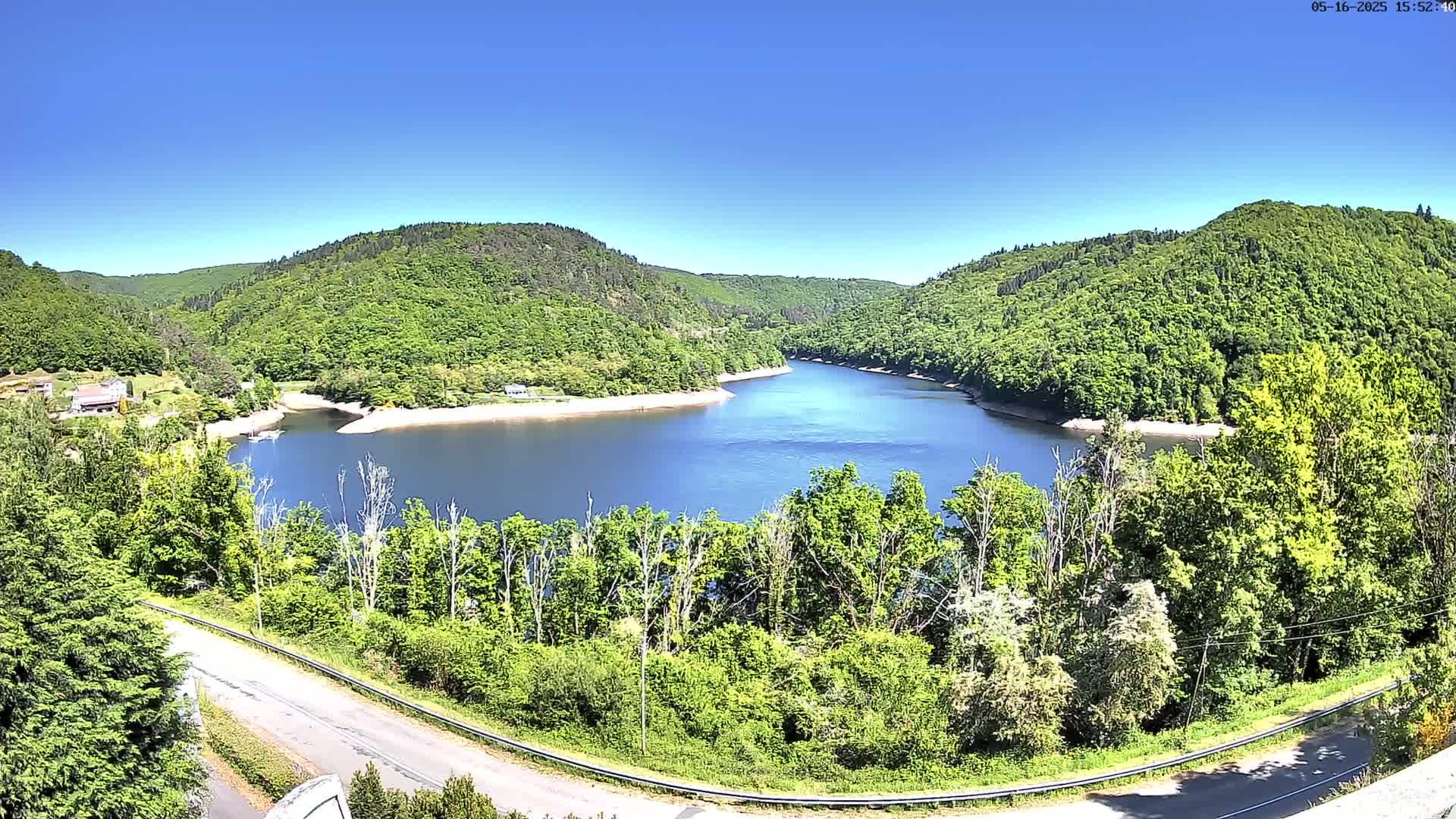A winding reservoir nestled in a valley of lush green, leafy hills under a clear blue sky.
