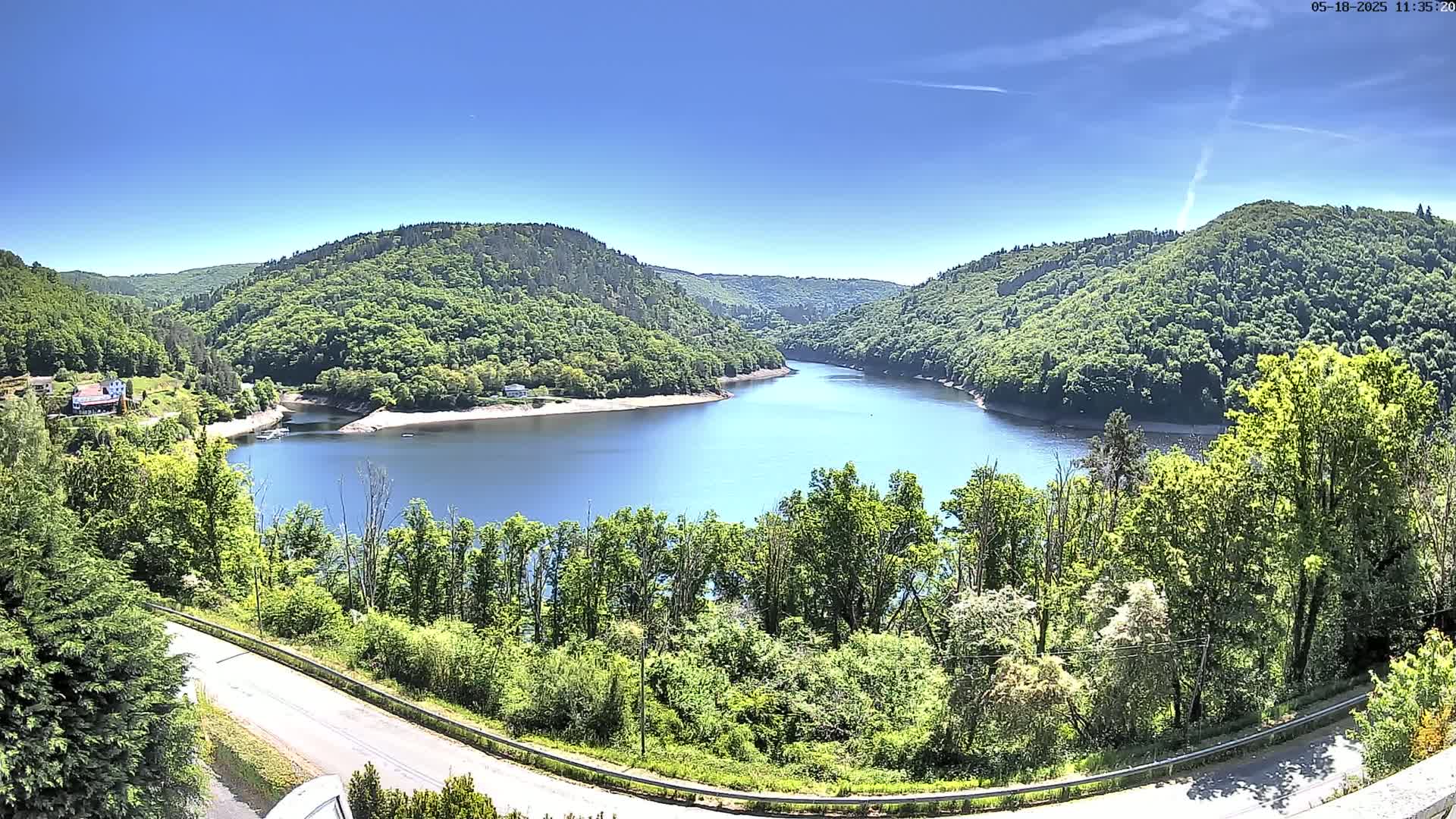A winding river surrounded by lush green hills and trees under a clear blue sky.