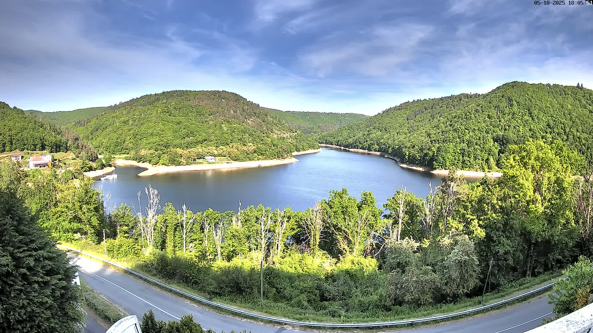 A winding river nestled in a valley of lush green hills under a mostly sunny sky.