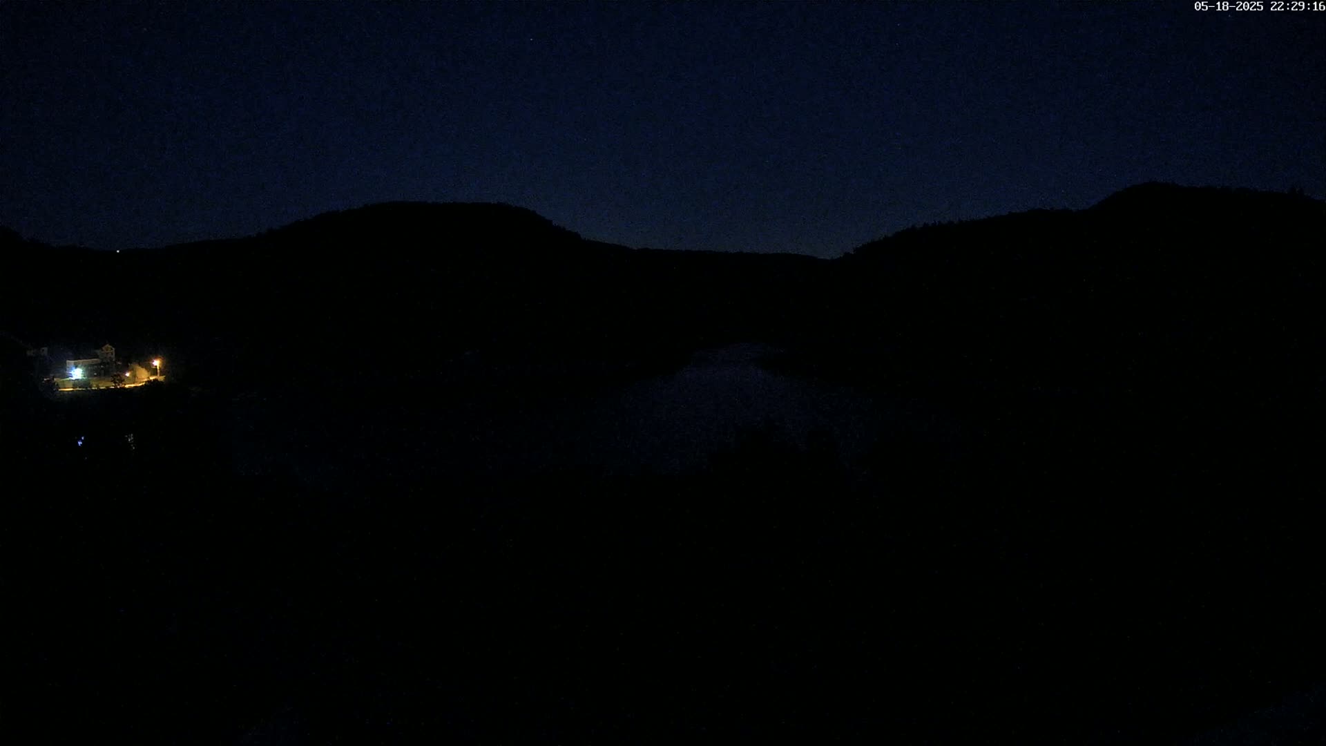 A dimly lit building is visible at the bottom of the image, nestled between dark, silhouetted hills under a clear, night sky.