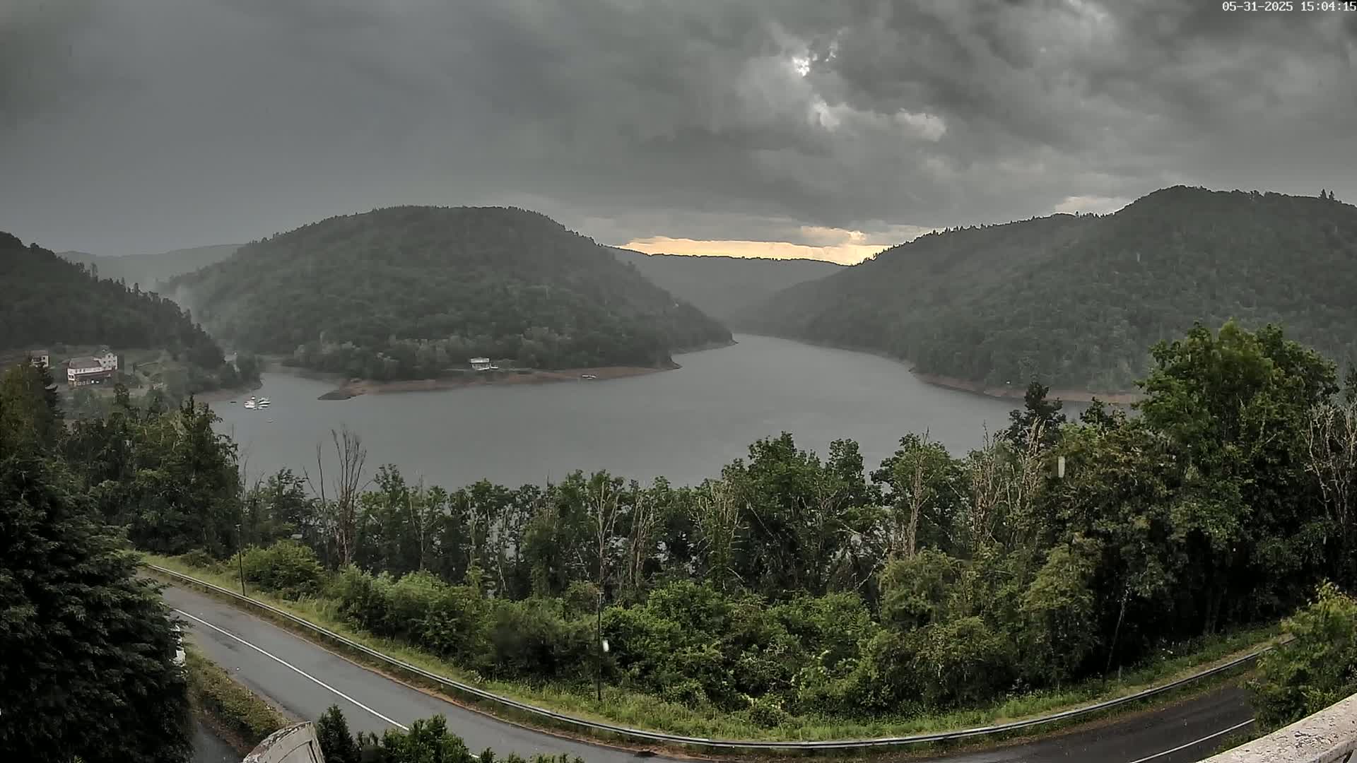 A lake nestled between dark green, forested hills under a stormy, gray sky.