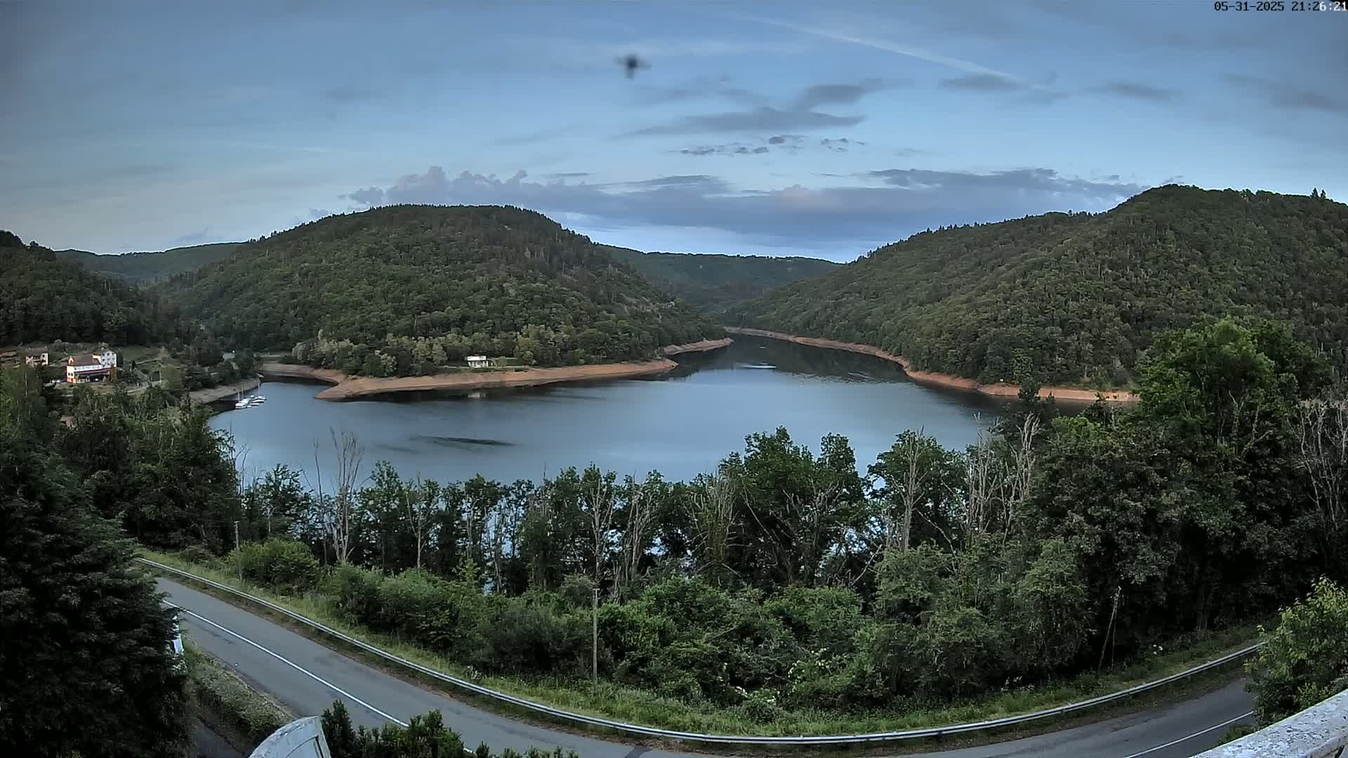 A calm lake nestled between lush green hills under a partly cloudy twilight sky.