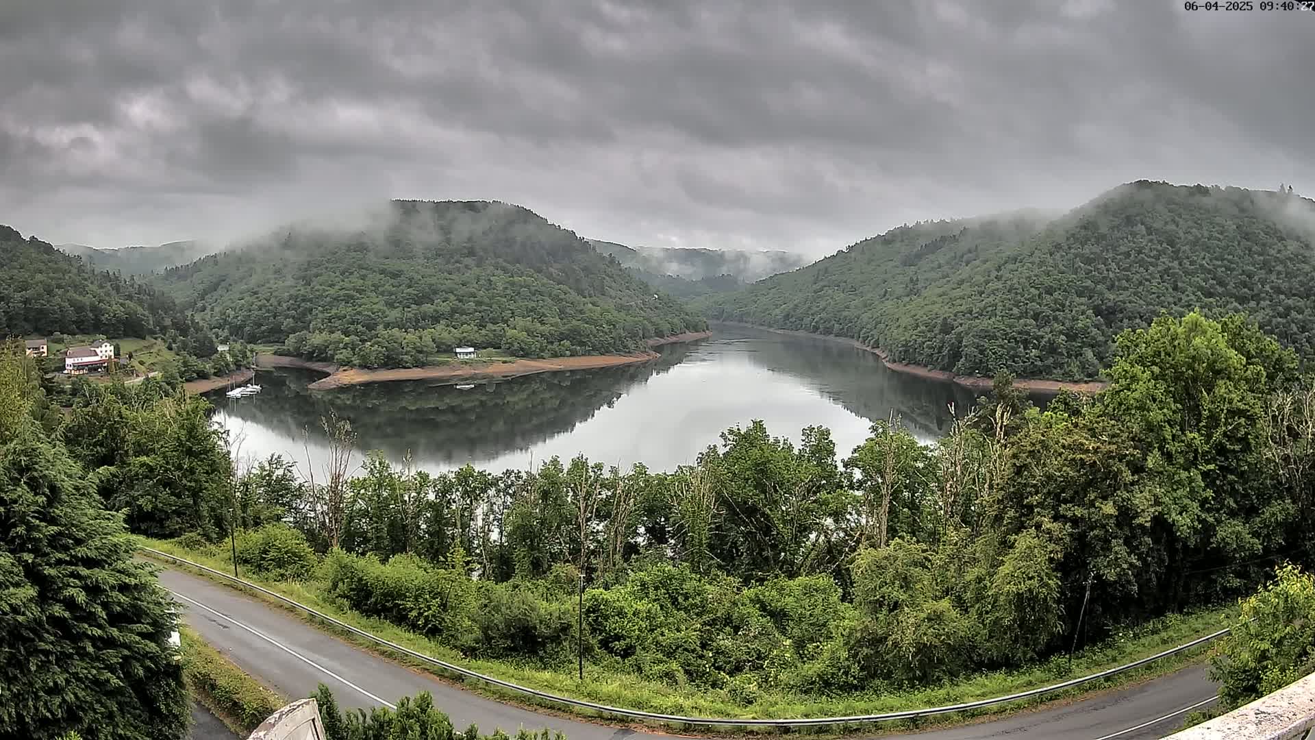 A calm river curves through a valley of lush green hills under a cloudy, overcast sky.