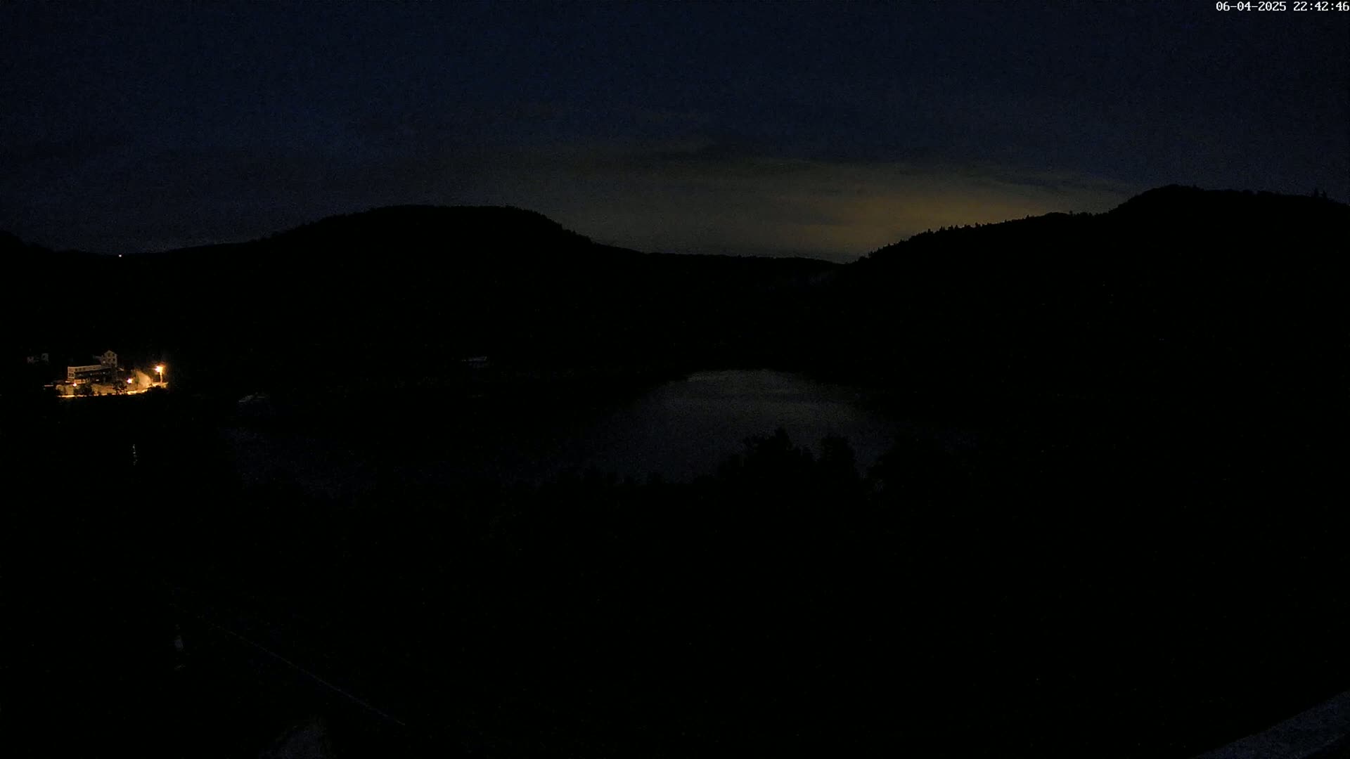 A dark, nighttime view of a body of water nestled between silhouetted hills under a mostly clear sky.