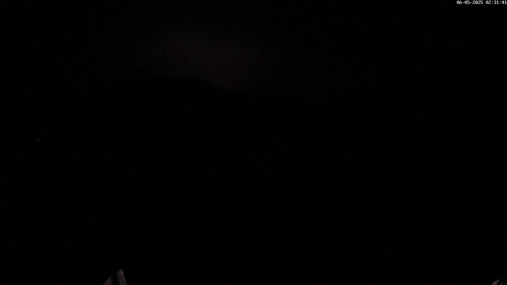 The image is almost entirely black, with a very faint, dark shape possibly suggesting a distant mountain range under a dark, nighttime sky.