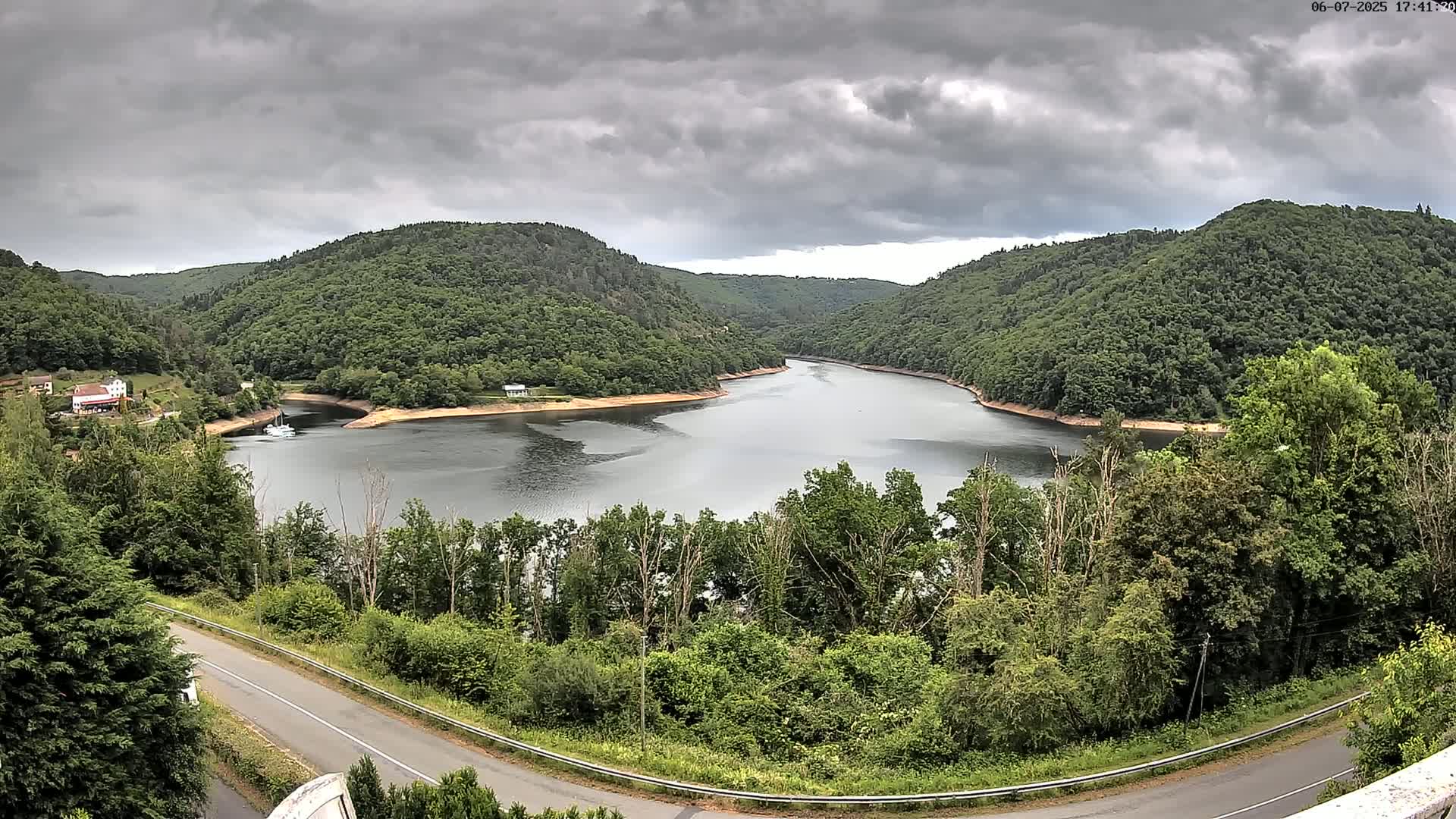 A winding river flows through a valley of lush green hills under a cloudy sky.