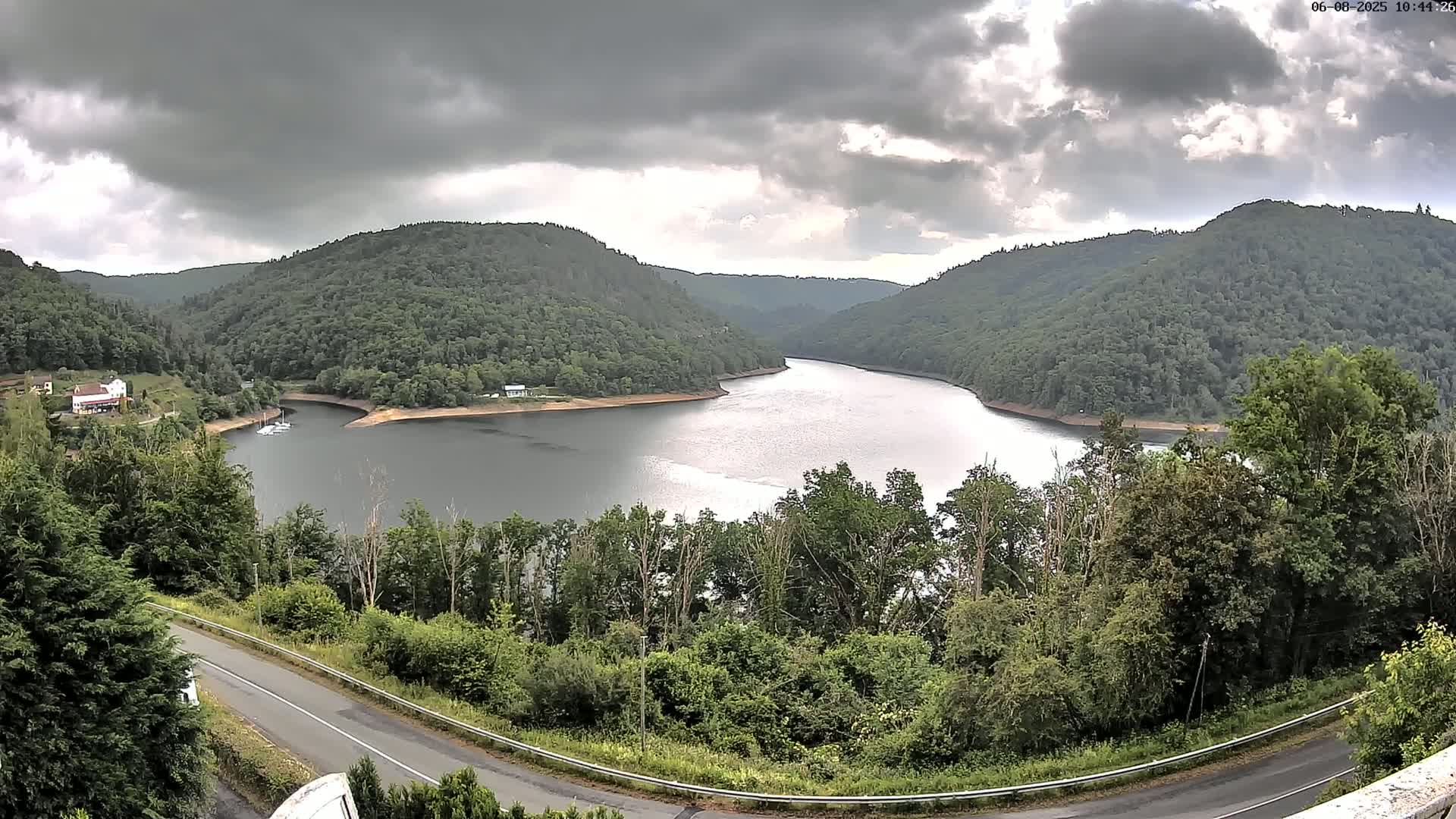 A winding river flows through a valley of lush green hills under a cloudy sky.