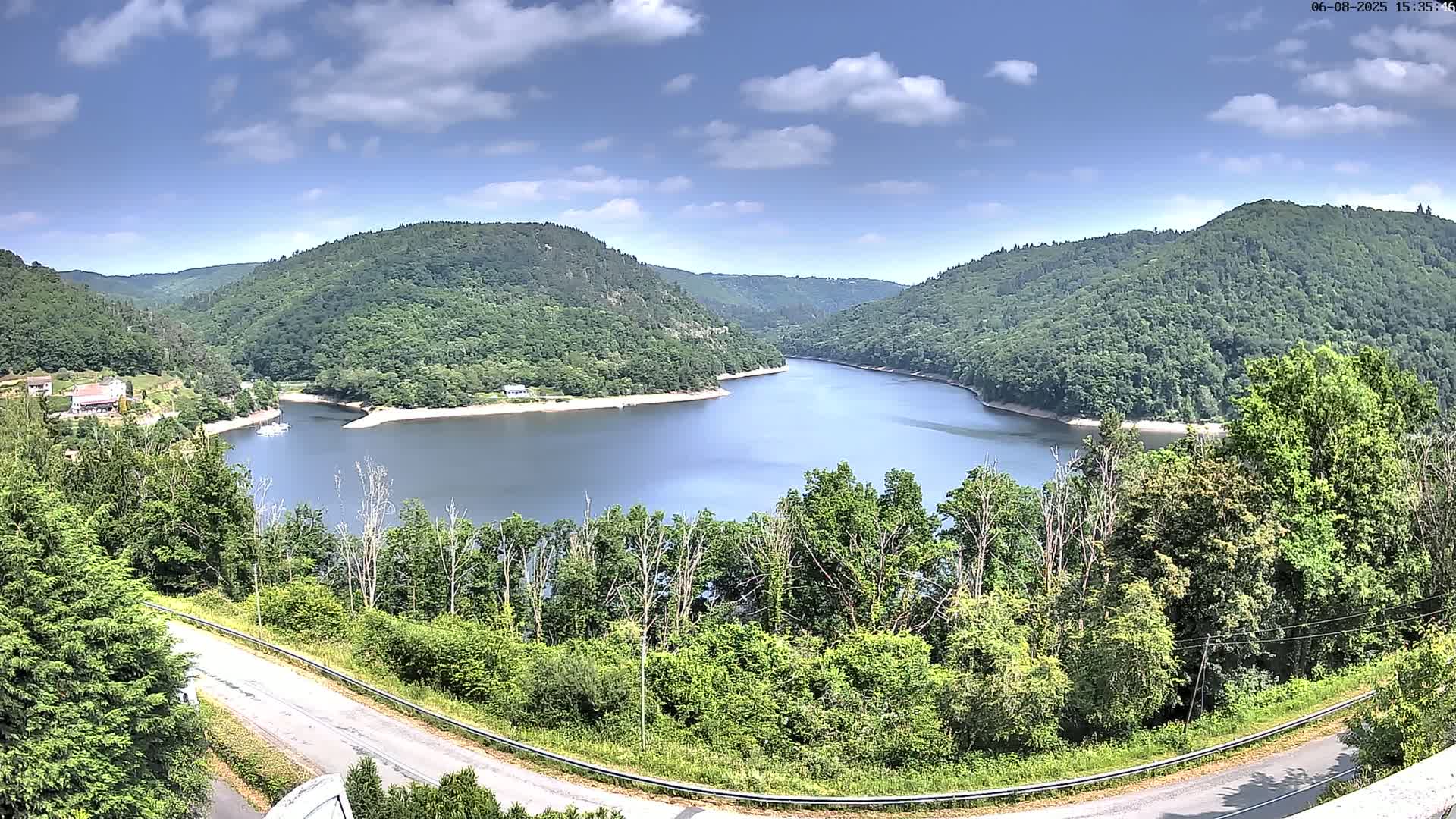 A curved lake nestled within a valley of lush green hills under a partly cloudy sky.