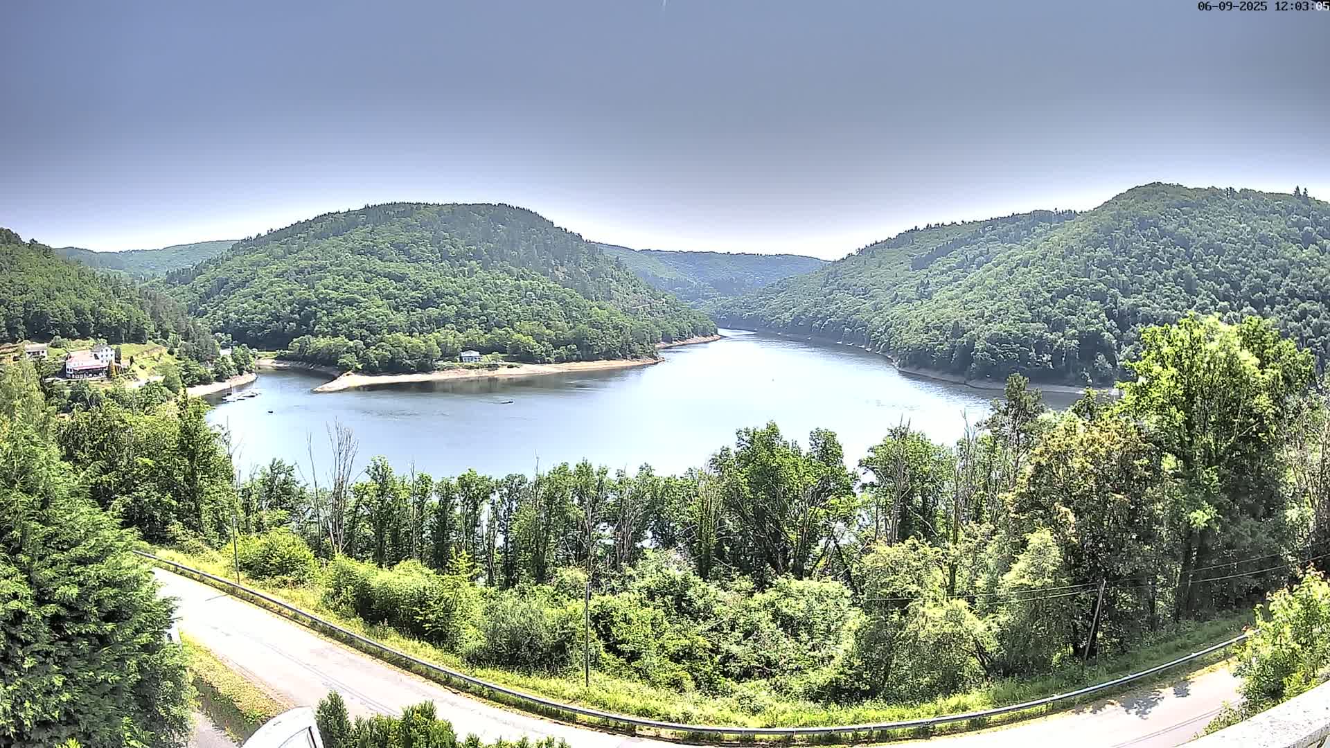 A calm lake nestled in a valley between lush green hills under a clear, bright sky.