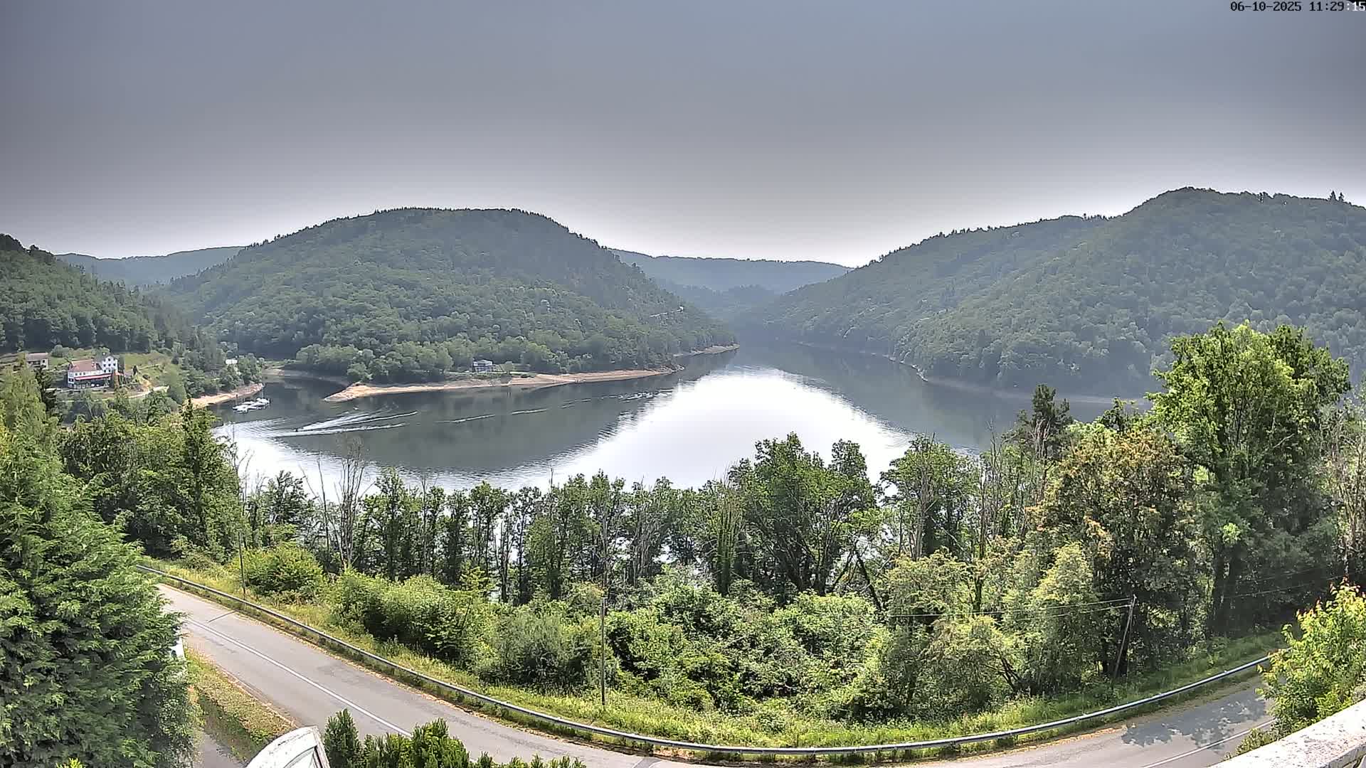 A calm lake nestled between verdant hills under a hazy sky.