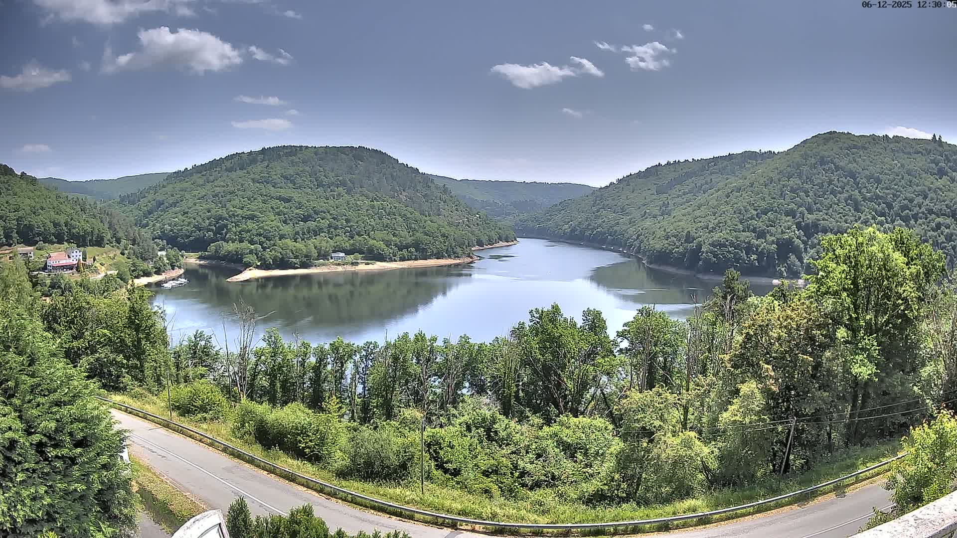 A tranquil lake curves between lush green hills under a partly cloudy sky.