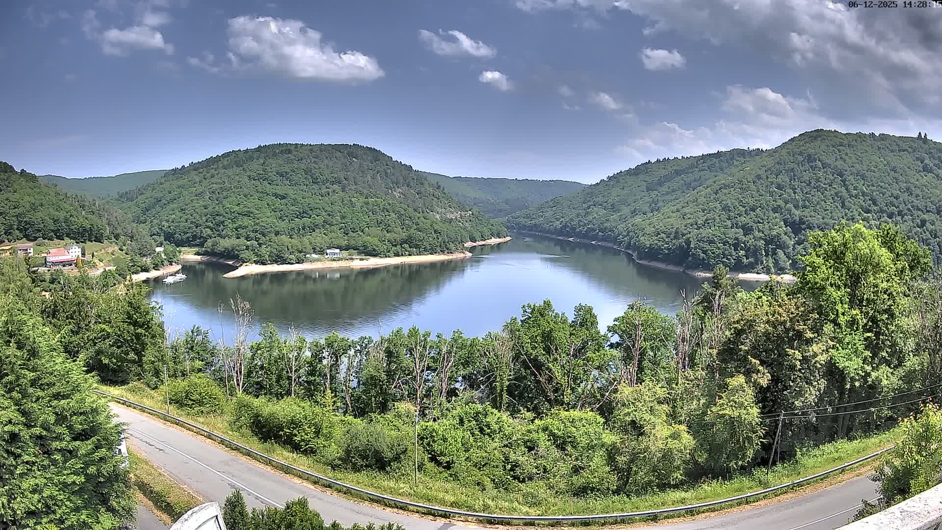 A partly cloudy sky overlooks a calm river curving through a lush green valley.