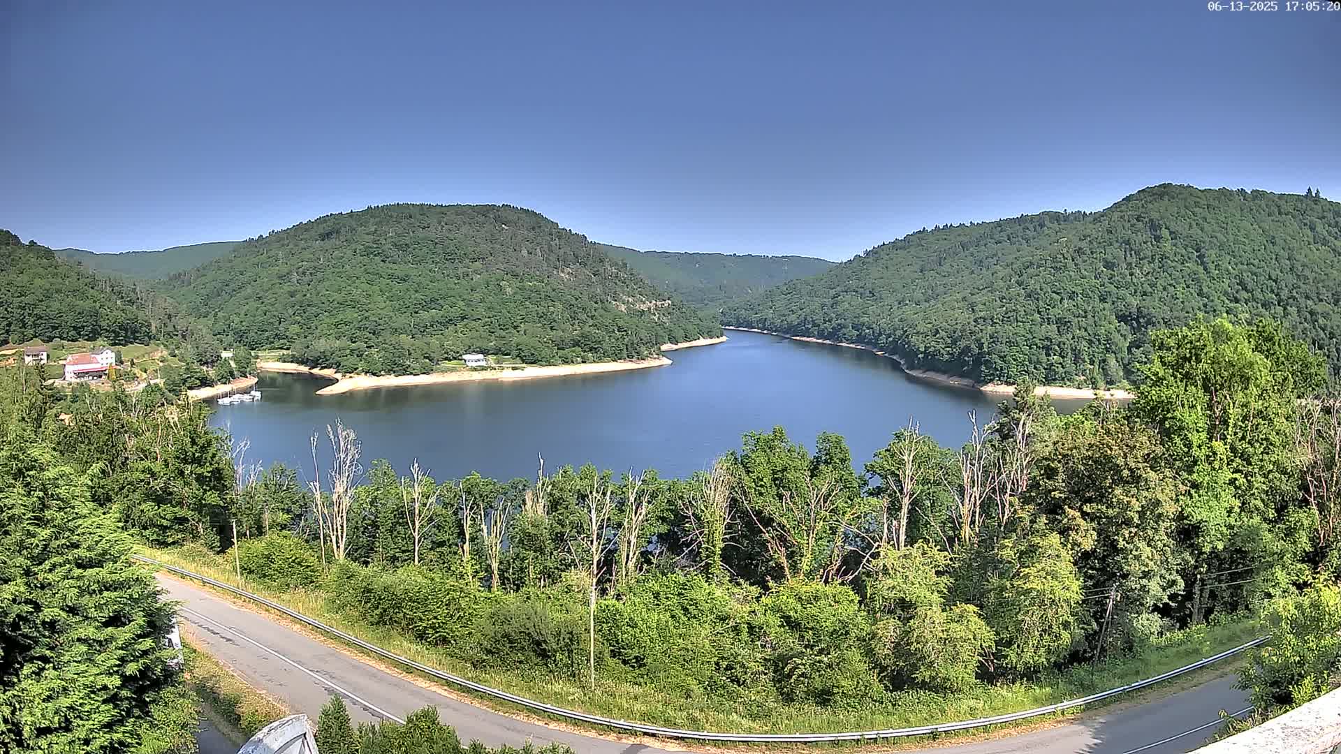 A curved lake nestled in a valley of lush green hills under a clear blue sky.