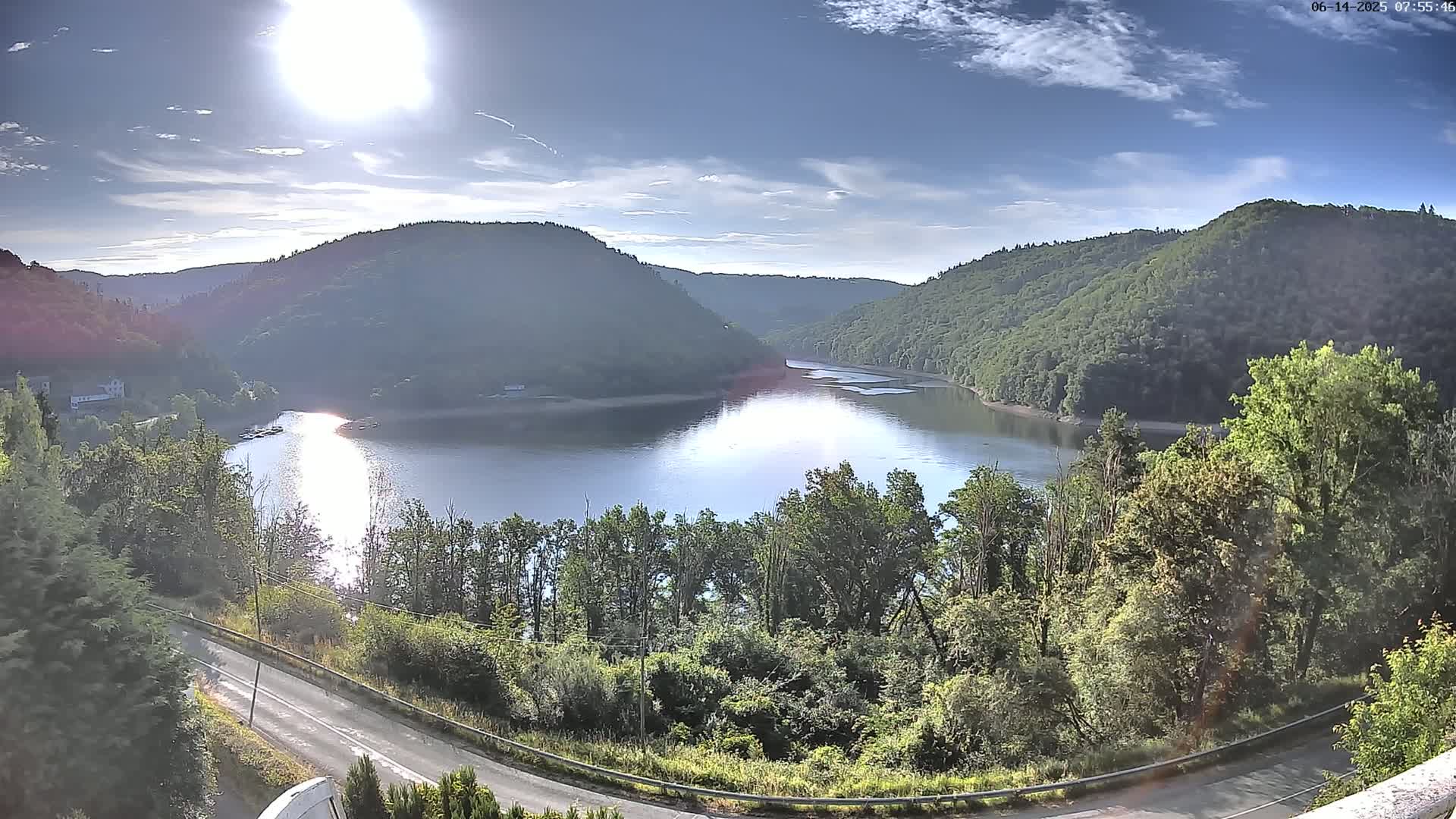 A curved lake nestled in a valley of lush green hills under a clear blue sky.