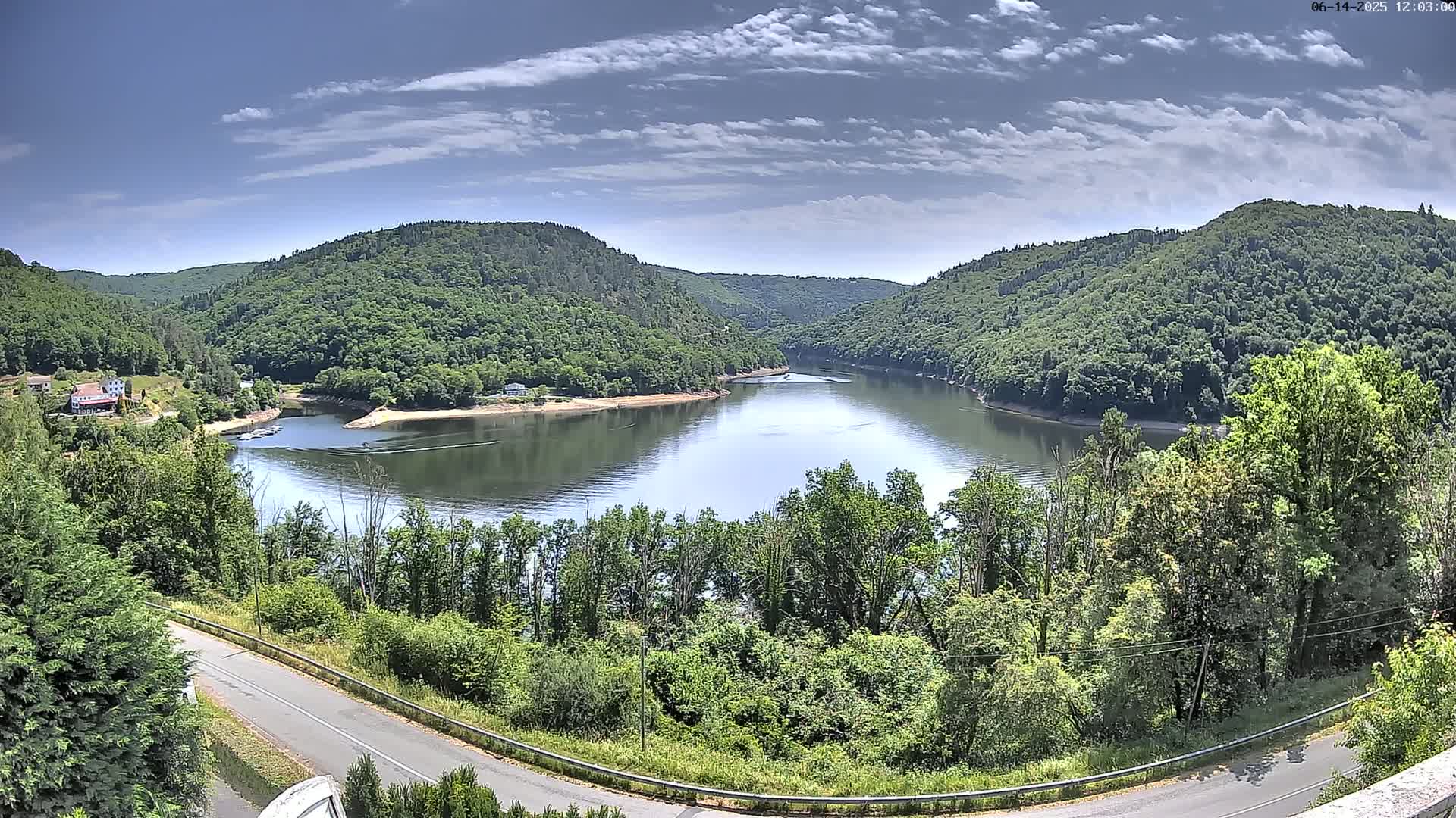 A calm river curves between lush green hills under a mostly sunny sky.