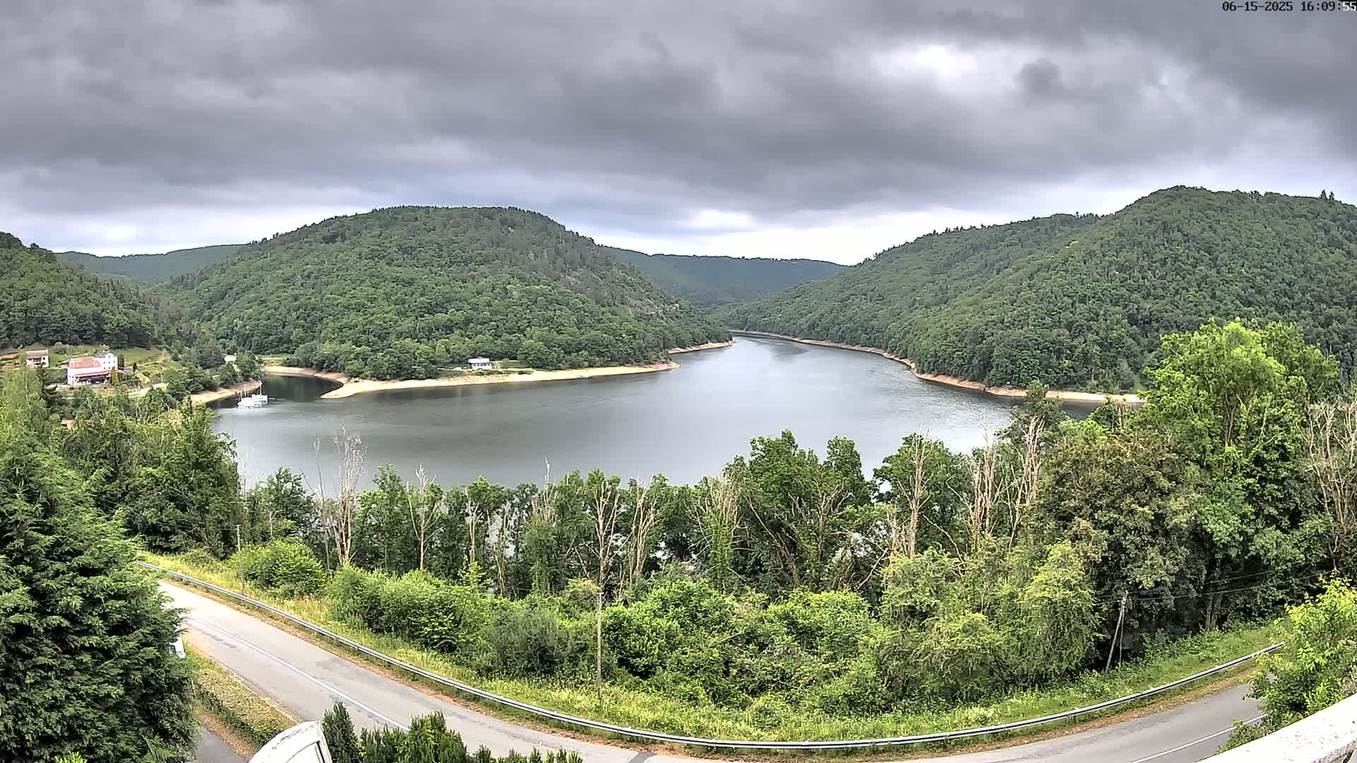 A horseshoe-shaped lake nestled between lush green hills under a cloudy sky.