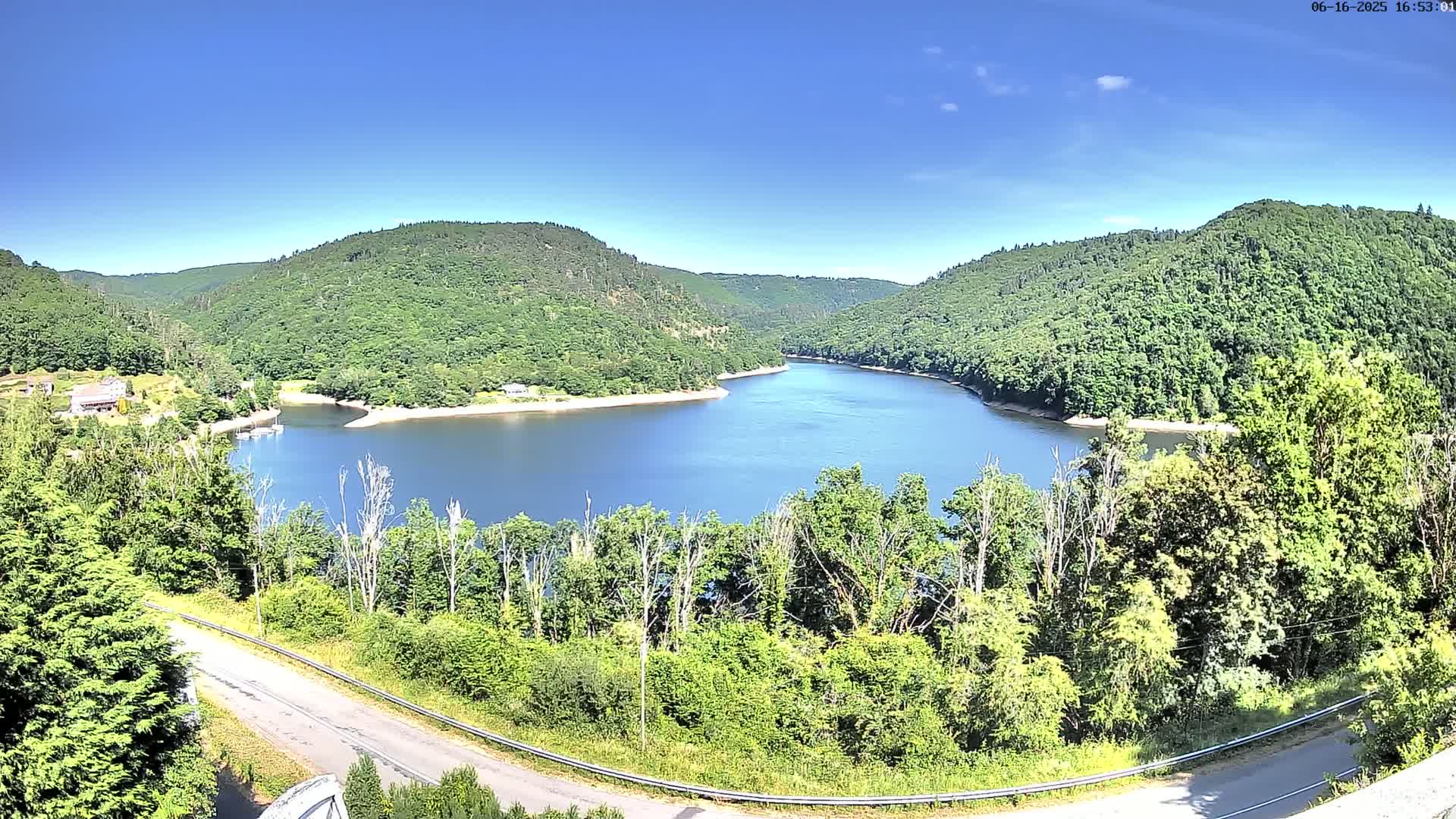 A curved lake nestled in a valley of lush green hills under a clear blue sky.