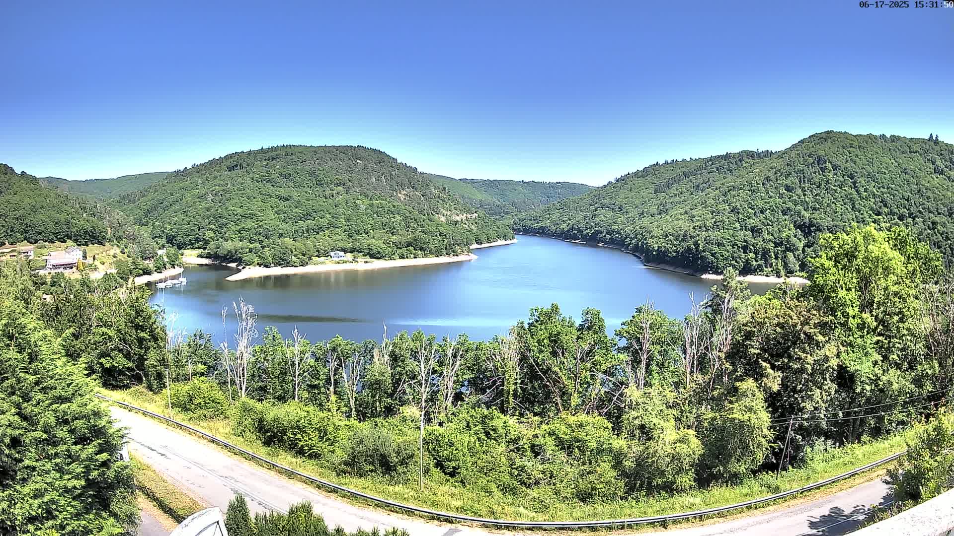 A tranquil lake nestled in a valley of lush green hills under a clear blue sky.