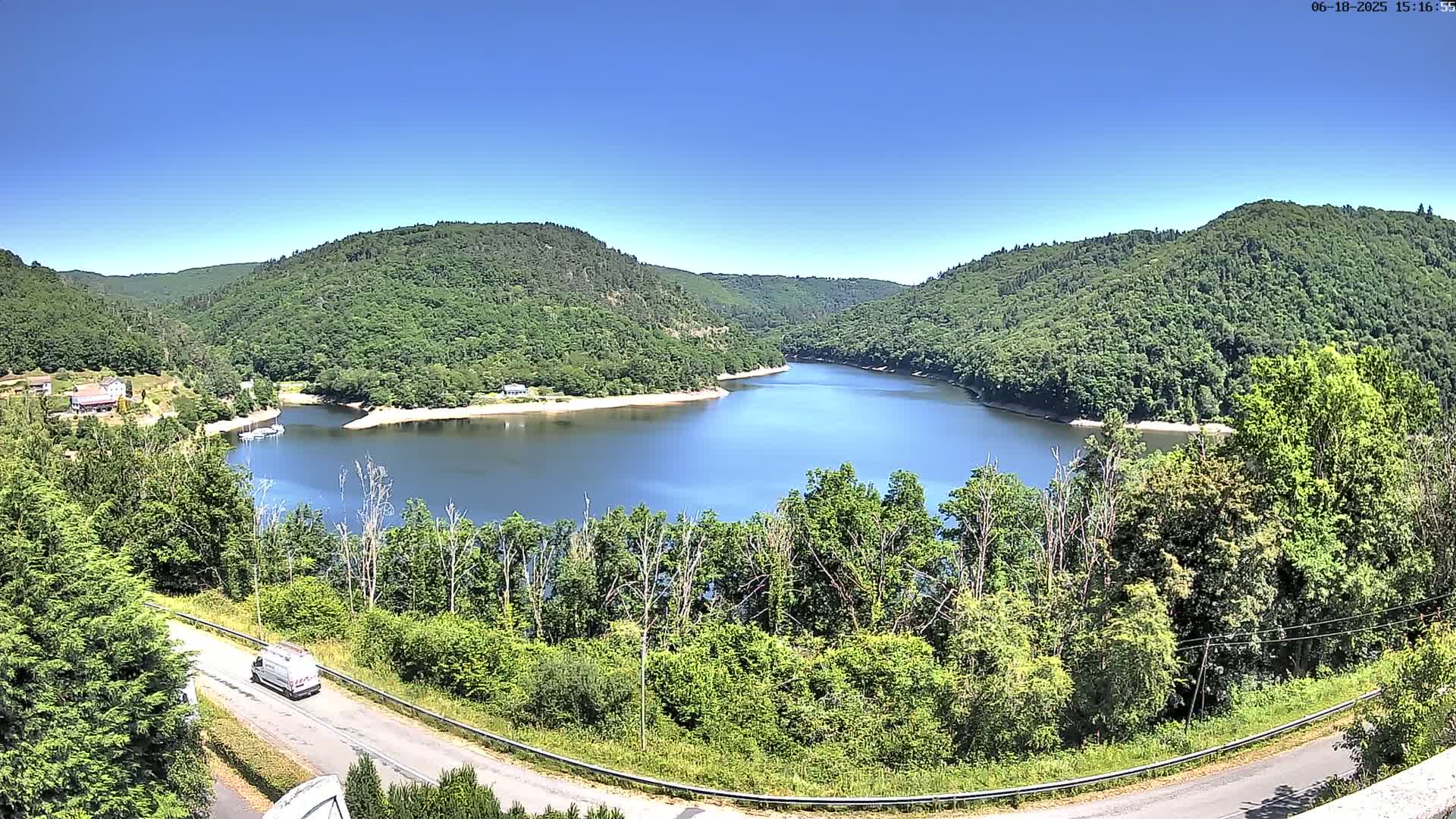 A winding reservoir nestled in a valley of lush green hills under a clear blue sky.