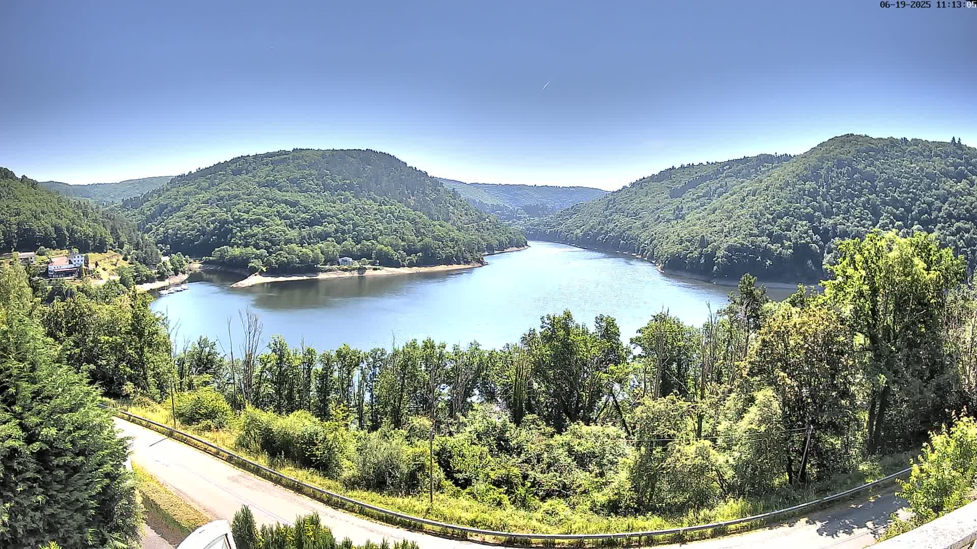 A winding river flows through a valley of lush green hills under a clear blue sky.