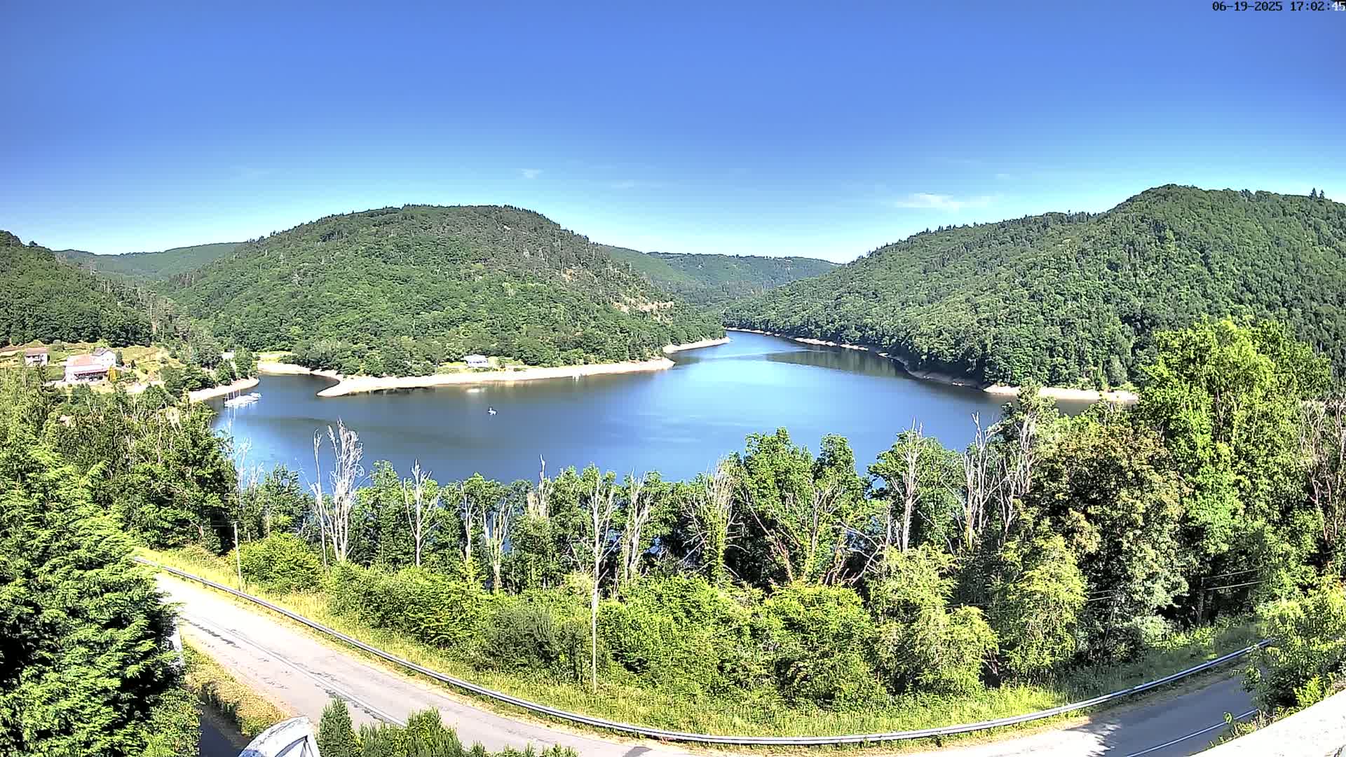 A curved lake nestled in a valley of lush green hills under a clear blue sky.