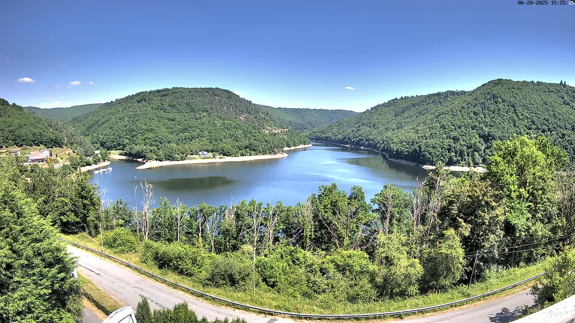 A calm, blue lake nestled in a valley surrounded by lush green hills under a clear blue sky.