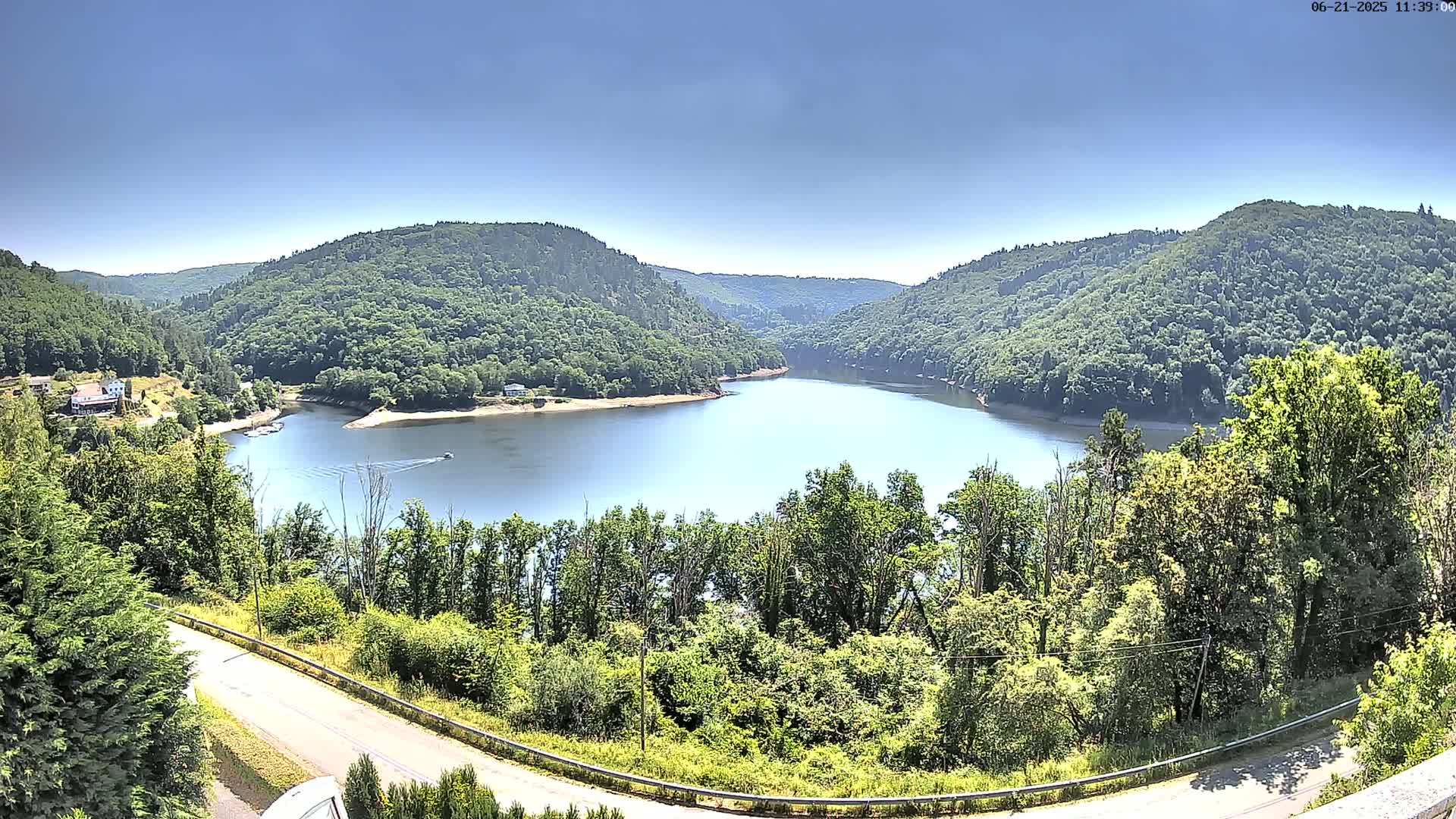 A calm lake nestled in a valley of lush green hills under a clear blue sky.