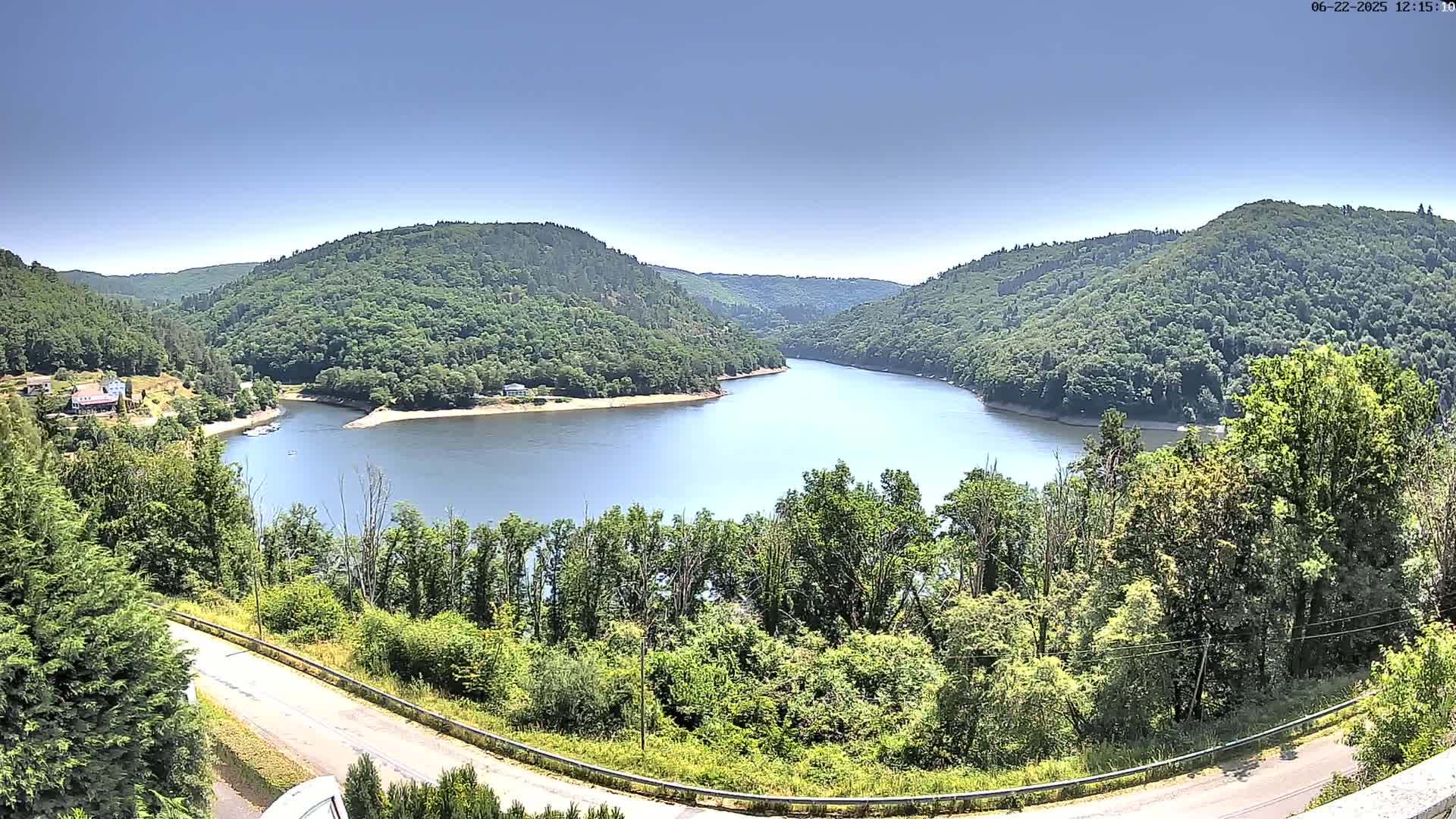 A winding river flows through a valley of lush green hills under a clear blue sky.