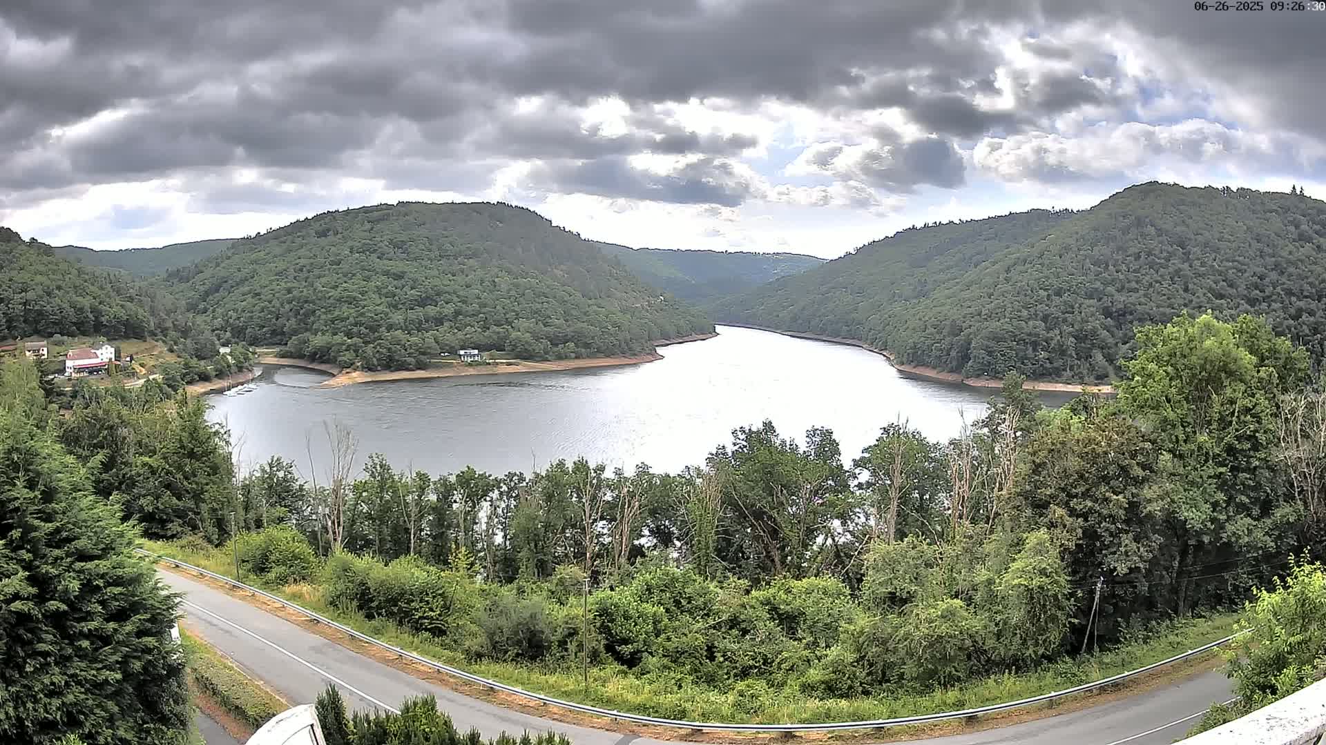A winding river flows through a valley of lush green hills under a partly cloudy sky.