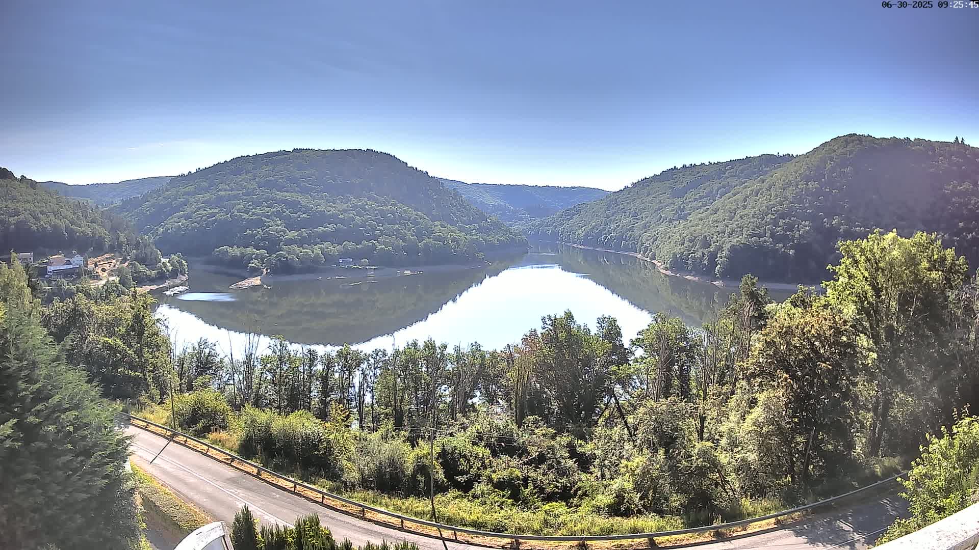 A calm lake nestled in a valley between verdant hills under a clear blue sky.