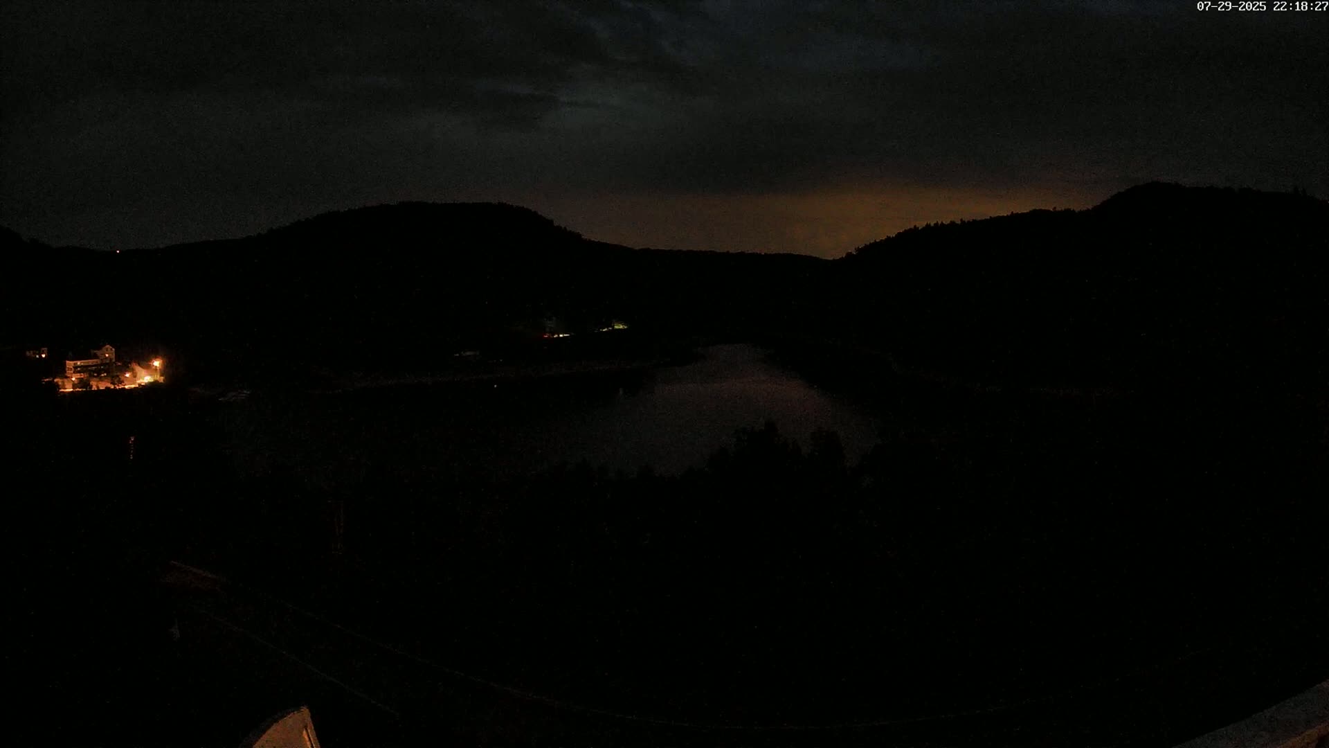 A nighttime view shows a dark, moonlit body of water nestled between dark hills under a cloudy sky.