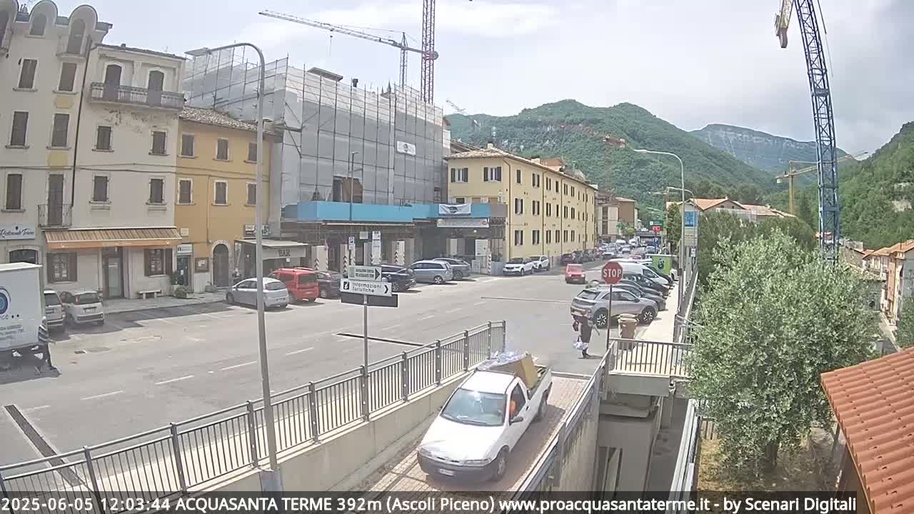 A town square with parked cars, buildings under construction, and a crane, all under sunny skies and clear weather.