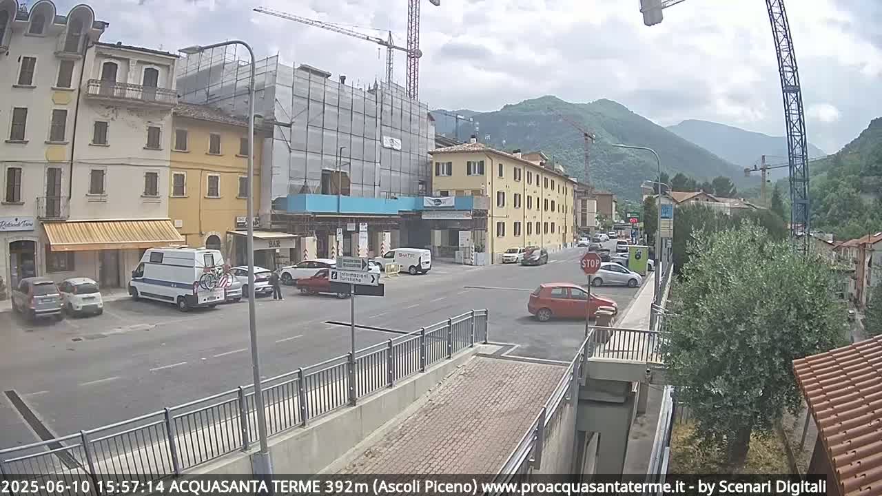 A partly cloudy day in a town nestled in a valley, with cars parked on the street and a building under construction.