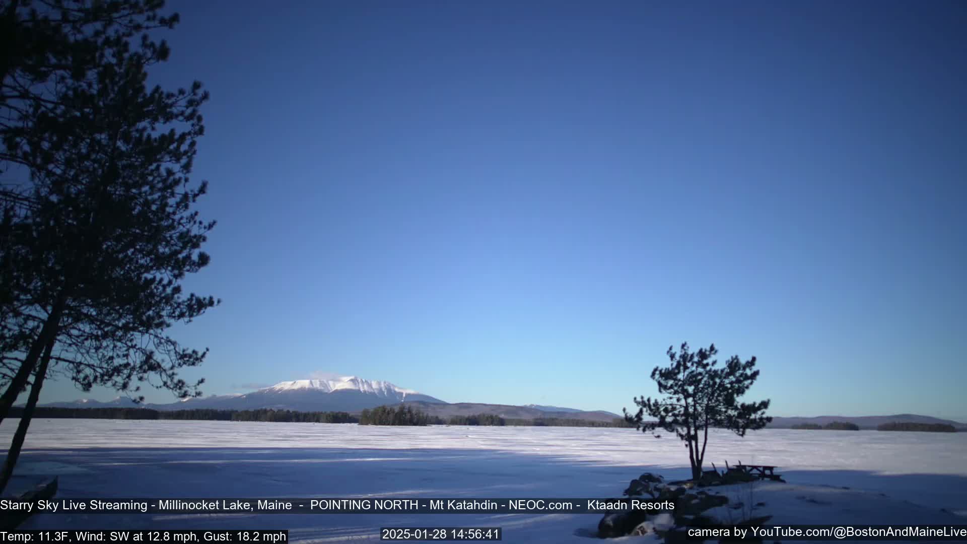 A snow-covered lake stretches to a distant, snow-capped mountain range under a clear blue sky.
