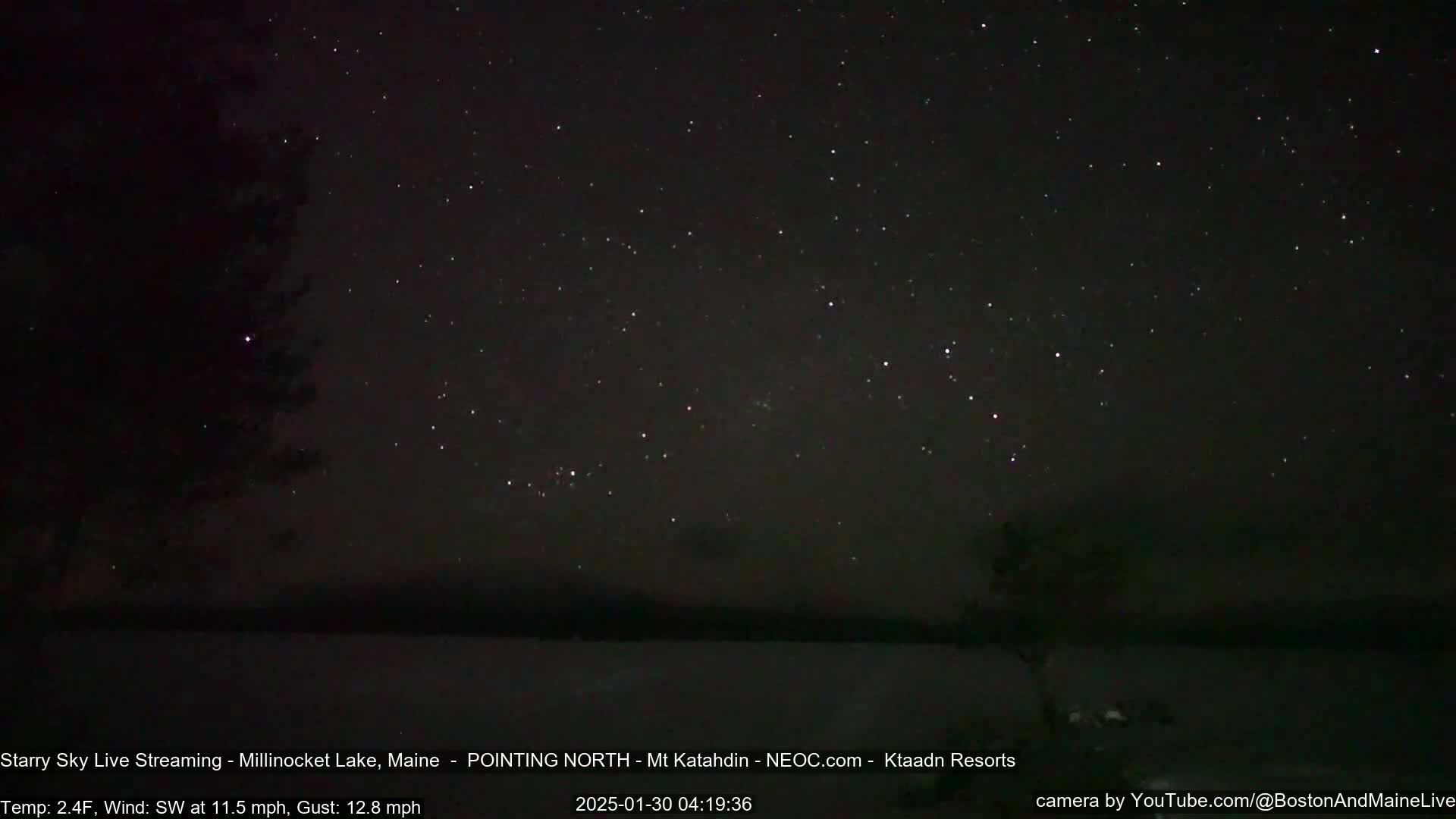 A night-time, outdoor scene shows a dark, starry sky over a snow-covered lake under a southwest wind of 11.5 mph with gusts up to 12.8 mph and a temperature of 2.4°F.
